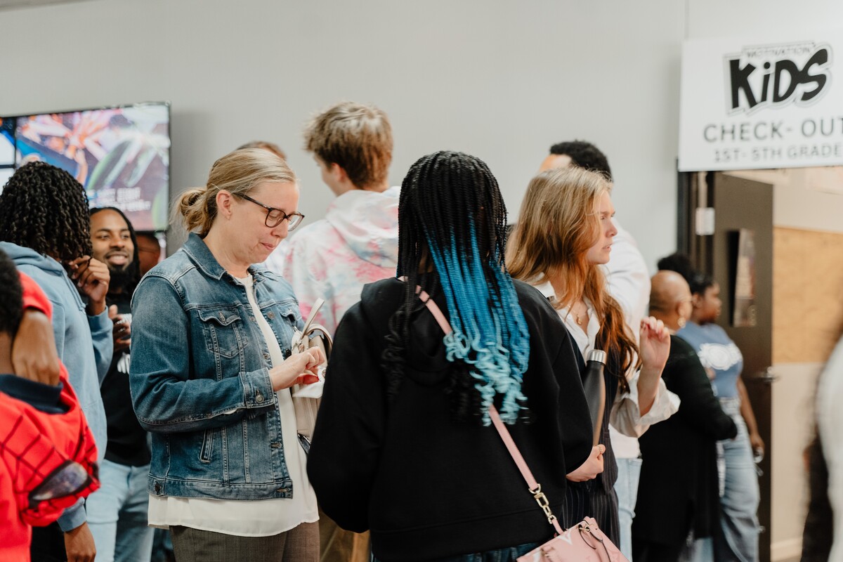 Group of people gathered indoors near a Kids Check-Out sign for 1st-5th grade.