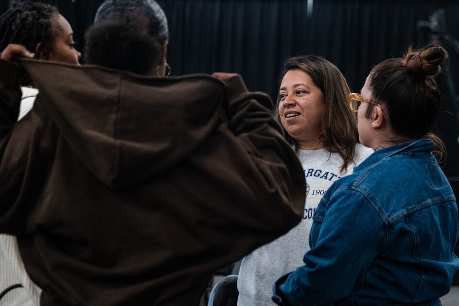 Group of four women engaged in a conversation indoors with a black curtain backdrop.