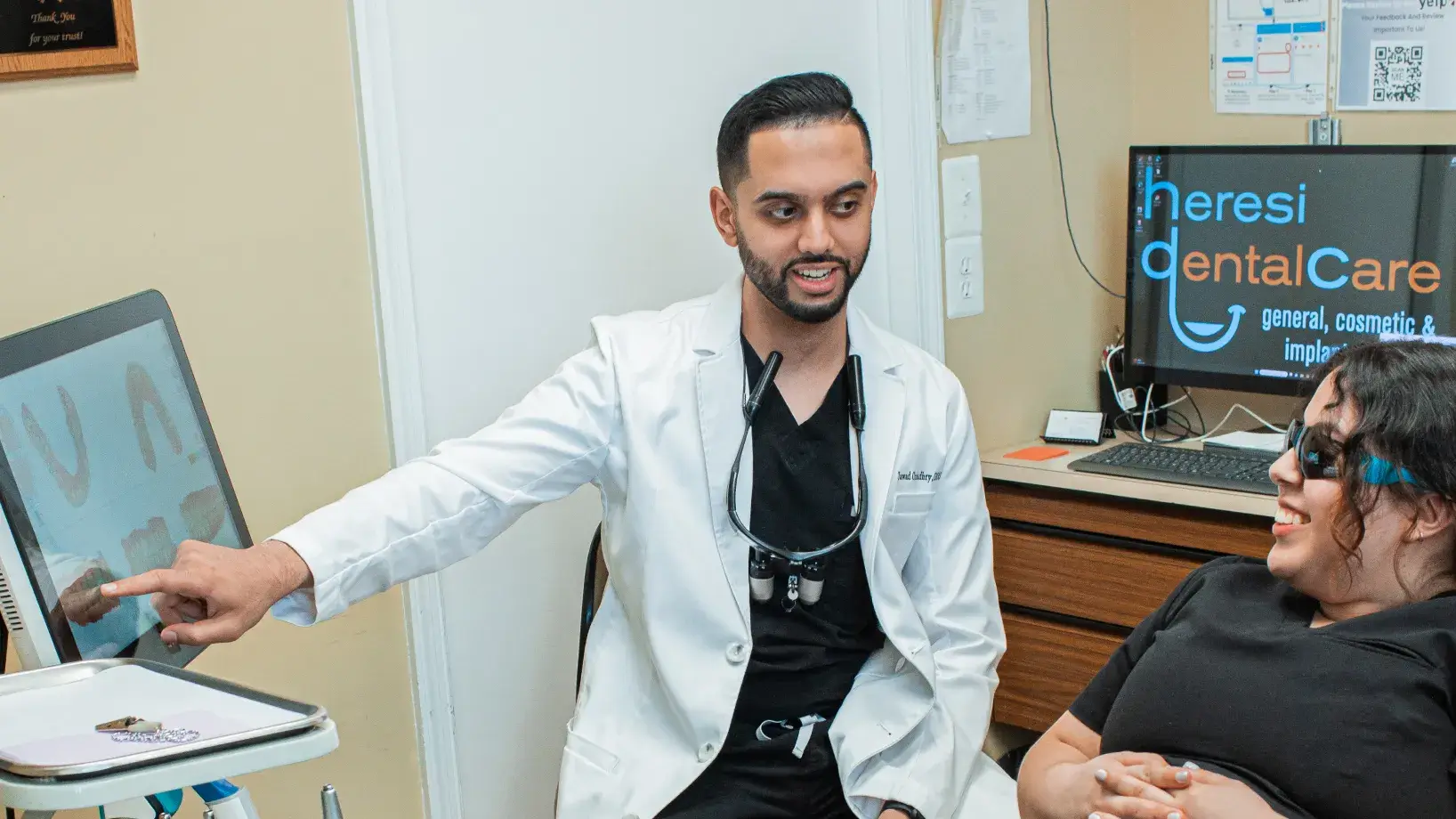 A man in a white lab coat pointing at a laptop screen.