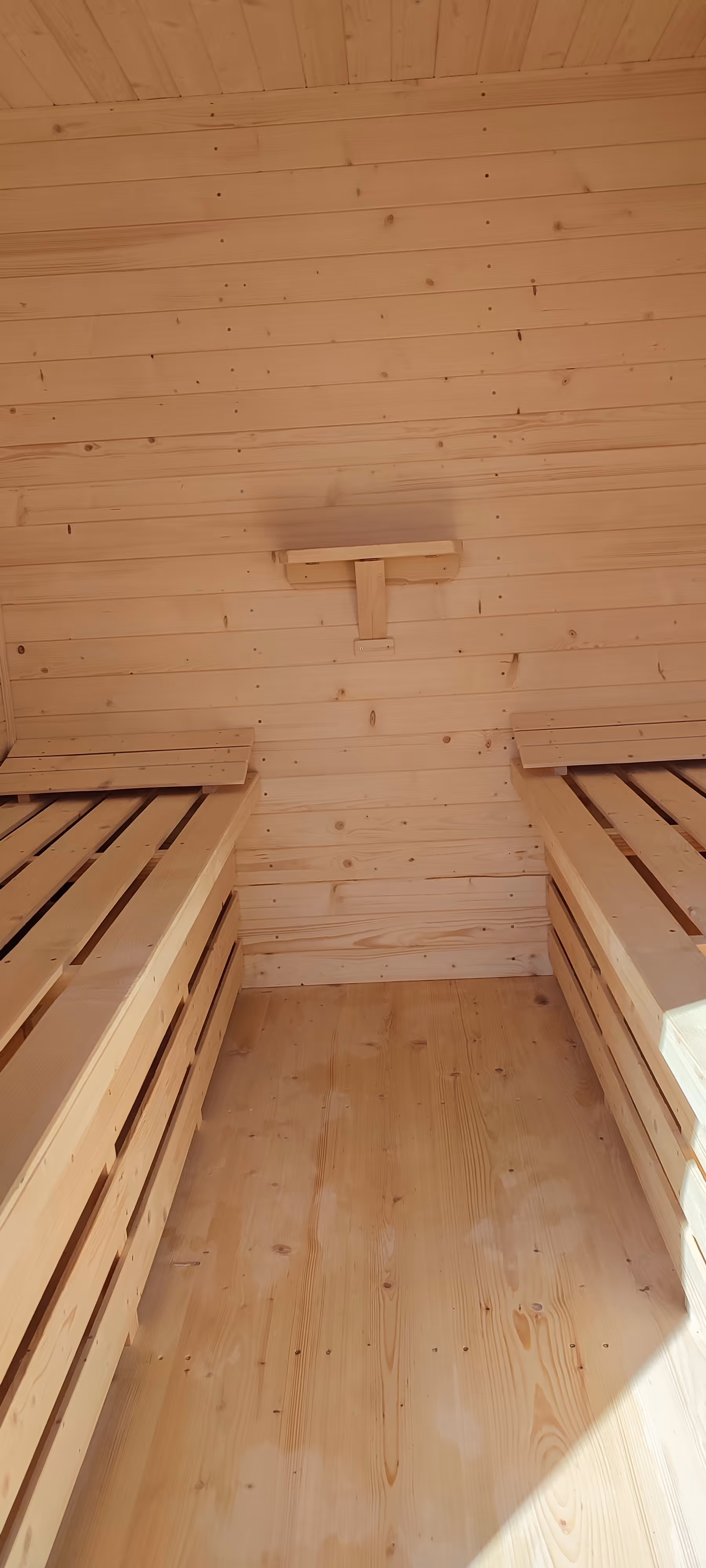 Wnętrze domku do apiterapii z dwiema drewnianymi leżankami po bokach i półeczką na ścianie.