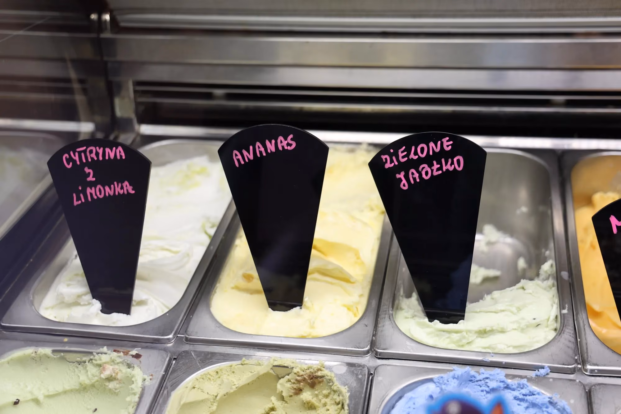 Kolorowe lody i sorbety o smakach cytryna z limonką, ananas oraz zielone jabłko w witrynie lodowej.