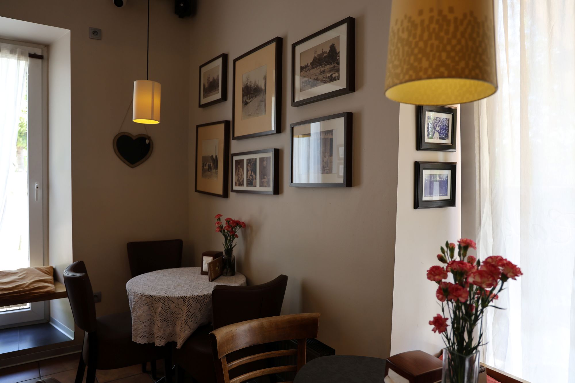 Przytulny stolik dla gości w Cafe Gidle z koronkowym obrusem i galerią historycznych fotografii na ścianie.