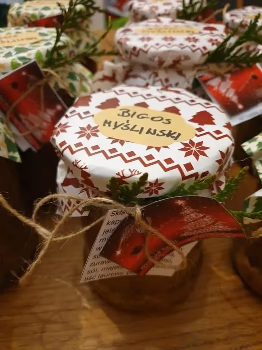 Słoik z bigosem, z wieczkiem przykrytym ozdobnym papierem w świąteczny wzór, przewiązany sznurkiem z etykietą i gałązką iglaka