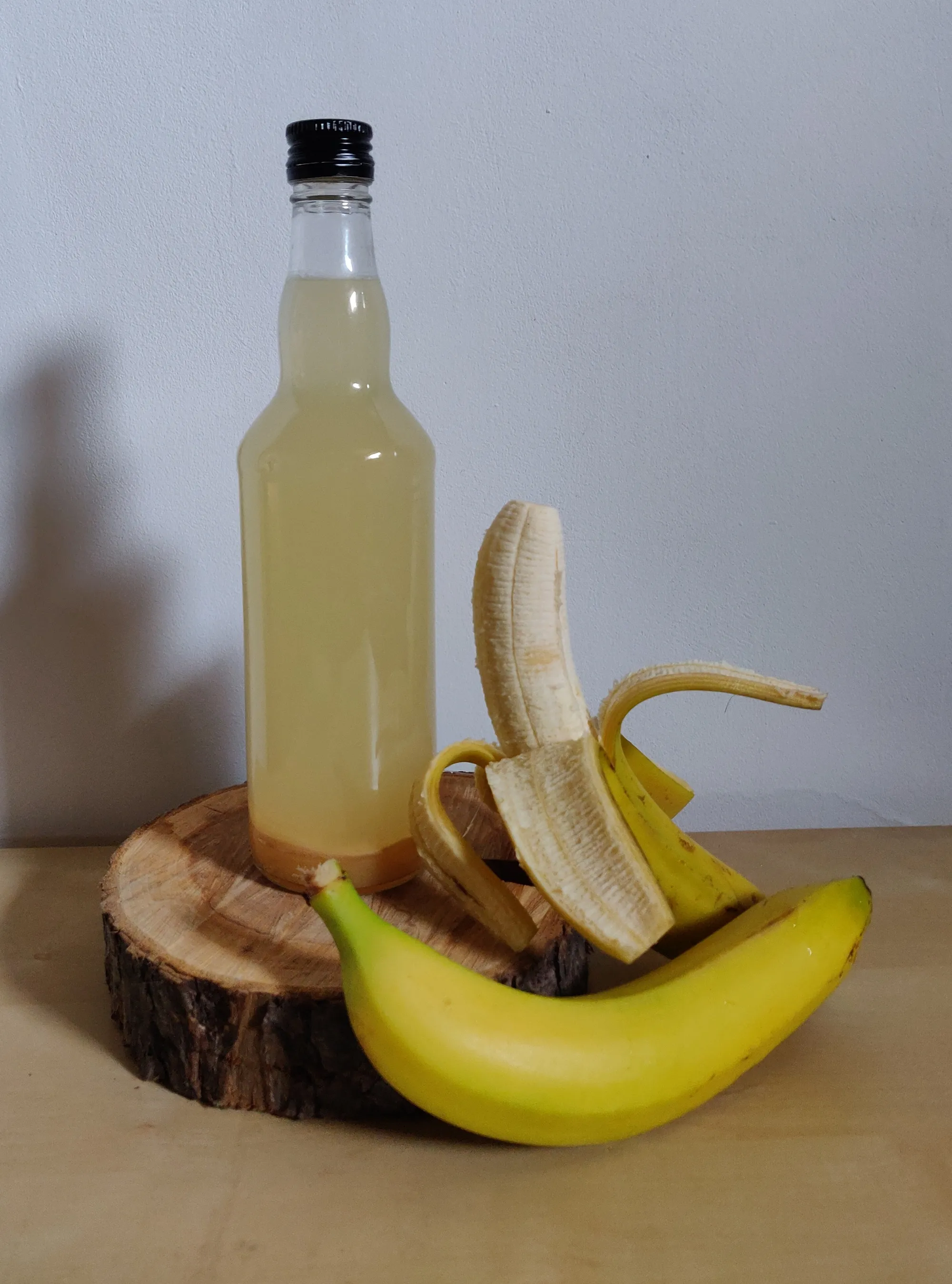 Szklana butelka z octem bananowym ustawiona na drewnianym plastrze obok świeżych bananów