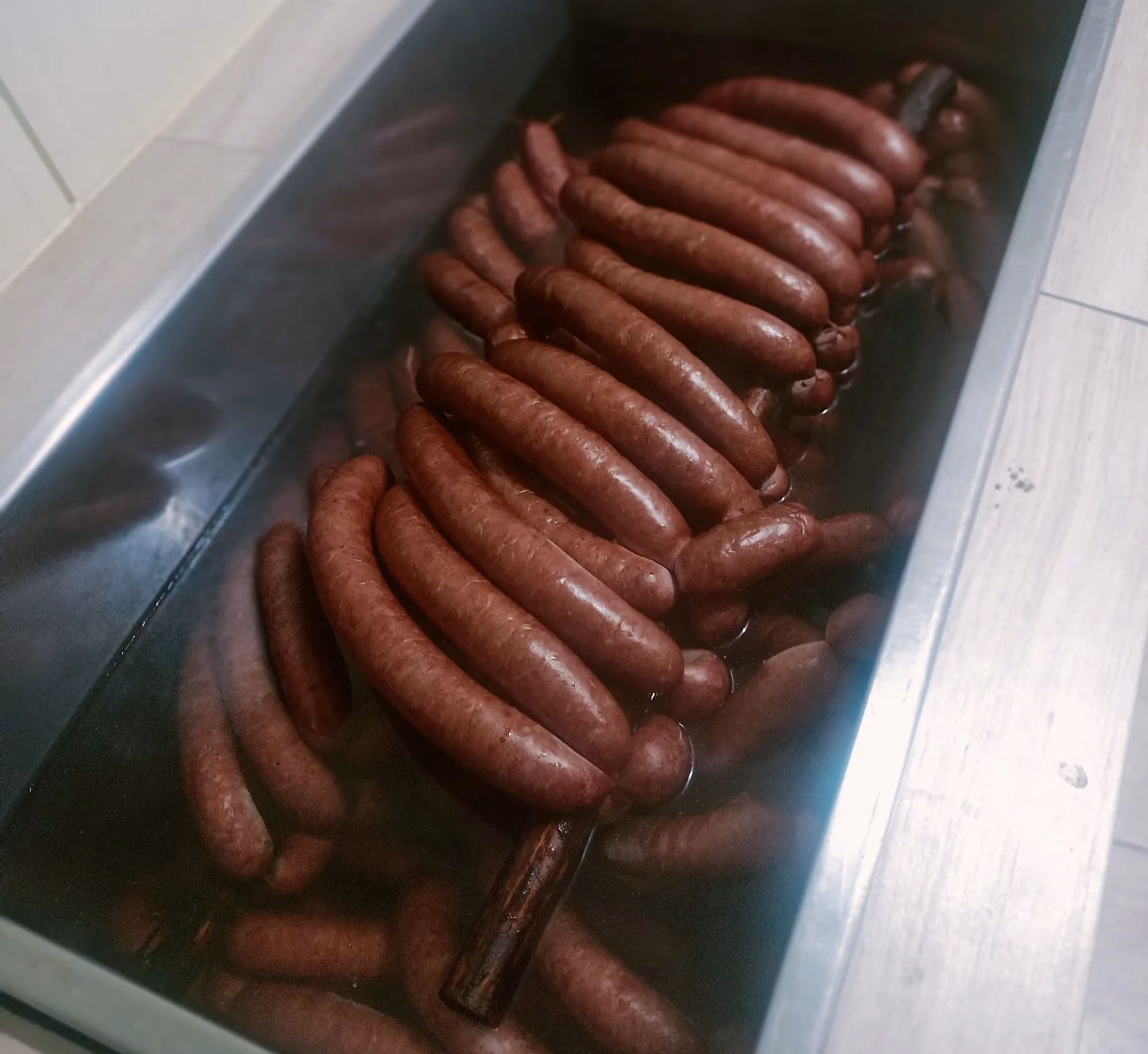 Kiełbasy zanurzone w gorącej wodzie, prawdopodobnie w procesie parzenia po wędzeniu