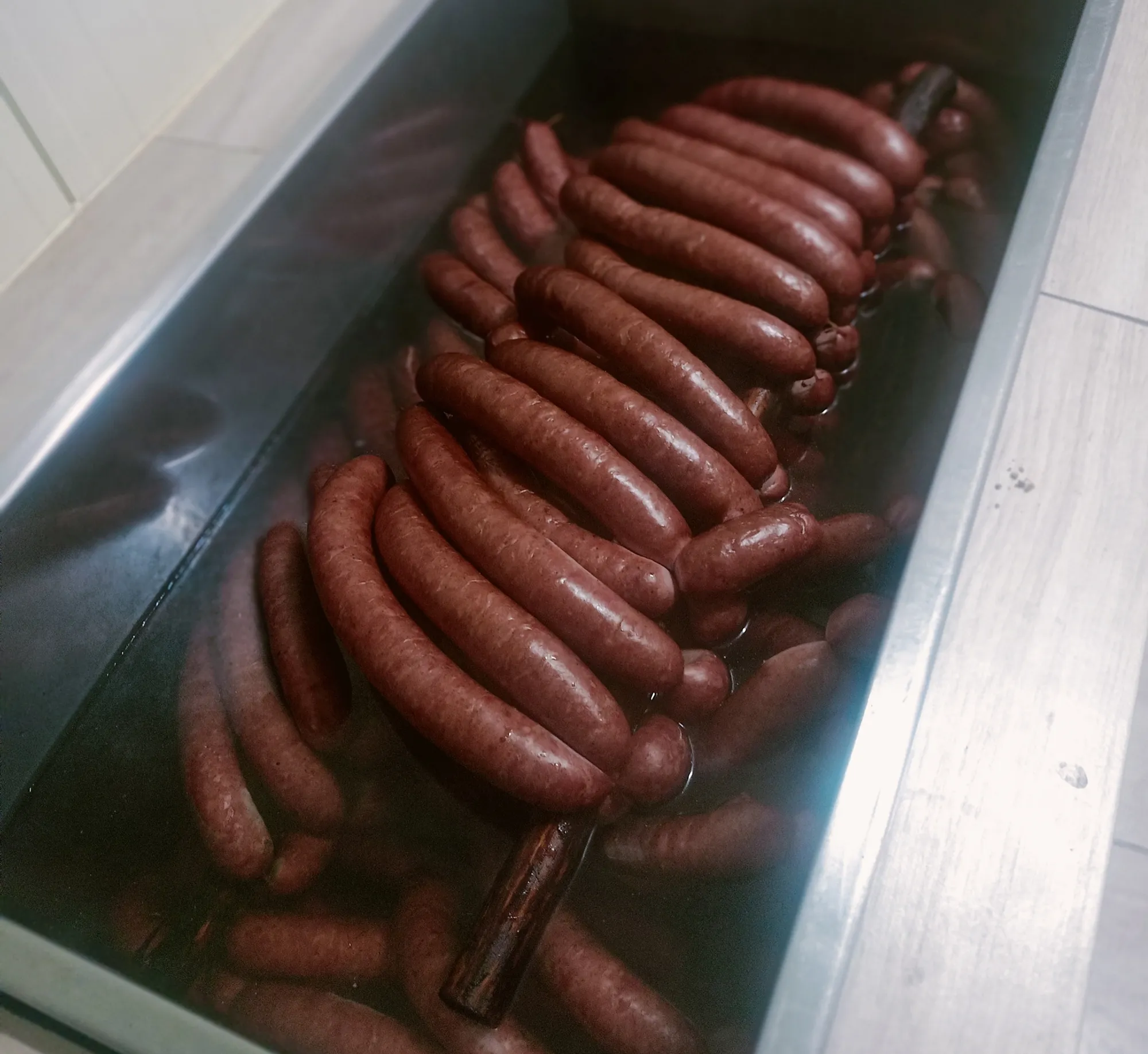 Kiełbasy zanurzone w gorącej wodzie, prawdopodobnie w procesie parzenia po wędzeniu