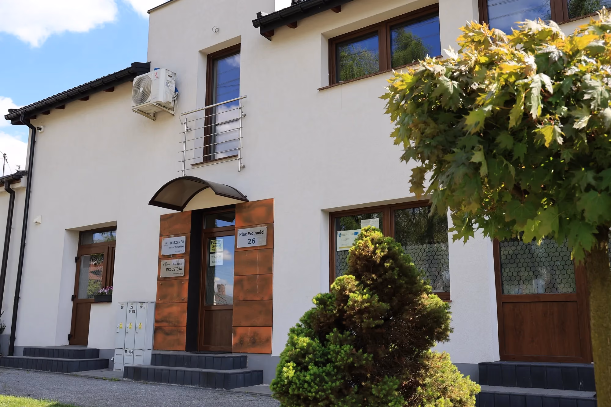 Budynek pasieki przy placu Wolności 26, z widocznym logo „Ojrzynek” oraz „Fundacja Karostoja”