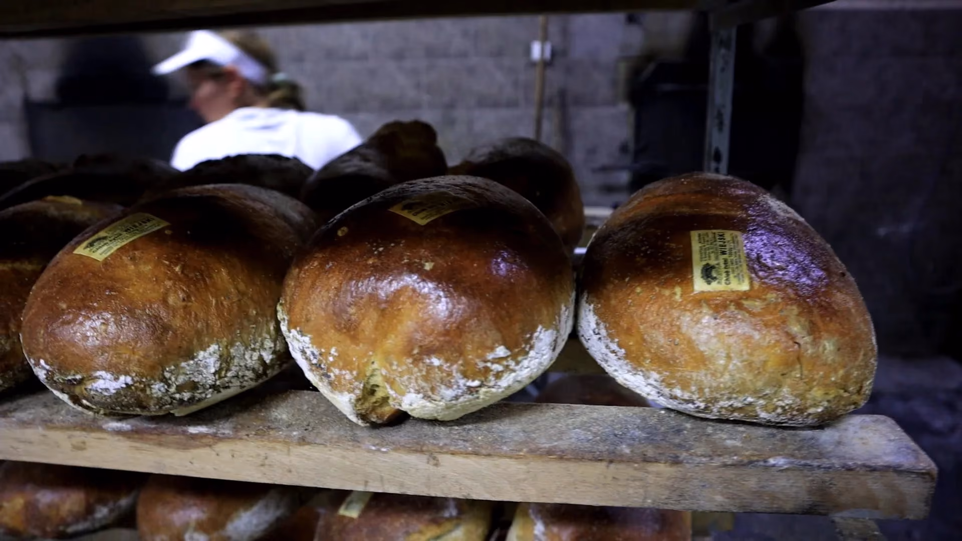Kilka upieczonych, prostokątnych chlebów foremkowych ułożonych w stos na jasnym tle. Bochenki mają mocno przypieczoną skórkę oprószoną mąką.