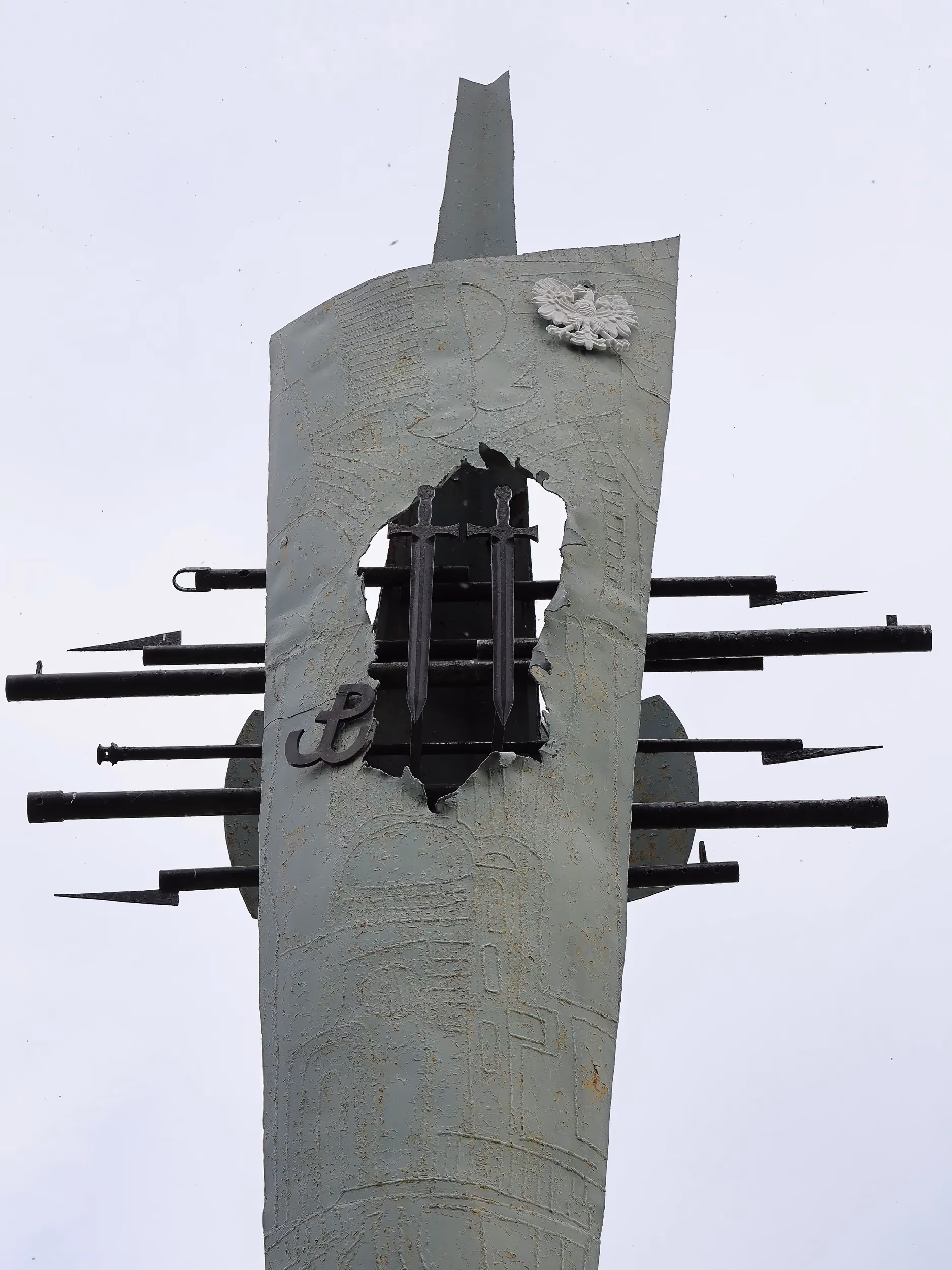 Zbliżenie na centralny element monumentu. W metalowej konstrukcji umieszczono symbol Polski Walczącej, dwa pionowe miecze oraz wizerunek orła. Kompozycja nawiązuje do walki o niepodległość i działalności polskiego ruchu oporu podczas II wojny światowej