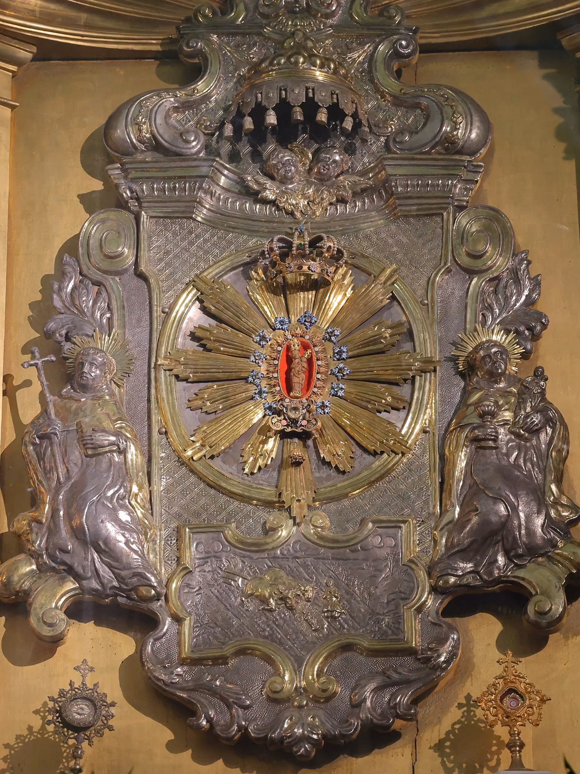 Zbliżenie centralnej części ołtarza z figurami świętych oraz otoczoną promienistą dekoracją figurką Matki Bożej z Dzieciątkiem.