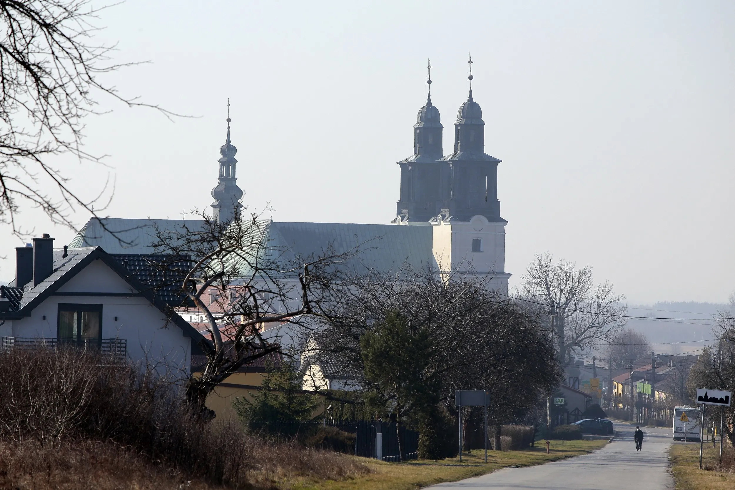 Widok na bazylikę w Gidlach z oddali. Nad zabudową miejscowości górują wieże i dach świątyni widoczne ponad drzewami i domami.