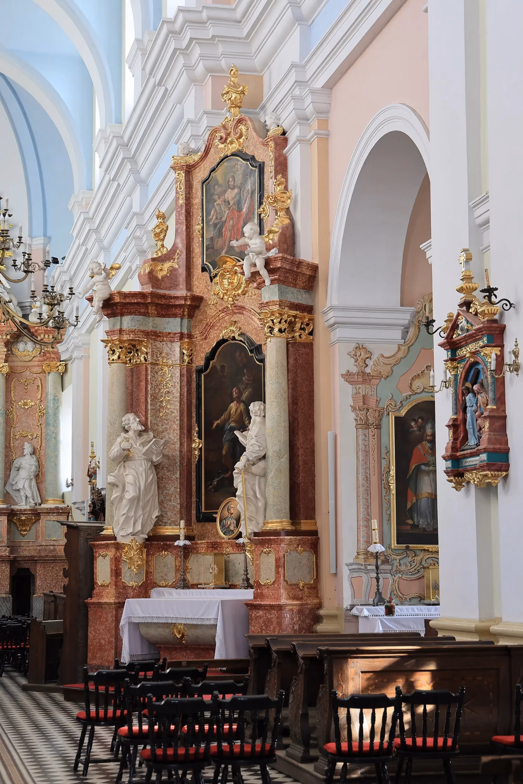 Barokowy boczny ołtarz z obrazami, rzeźbami i złoconymi zdobieniami. Przed ołtarzem ustawiono krzesła, a wnętrze rozświetla światło wpadające przez okna.