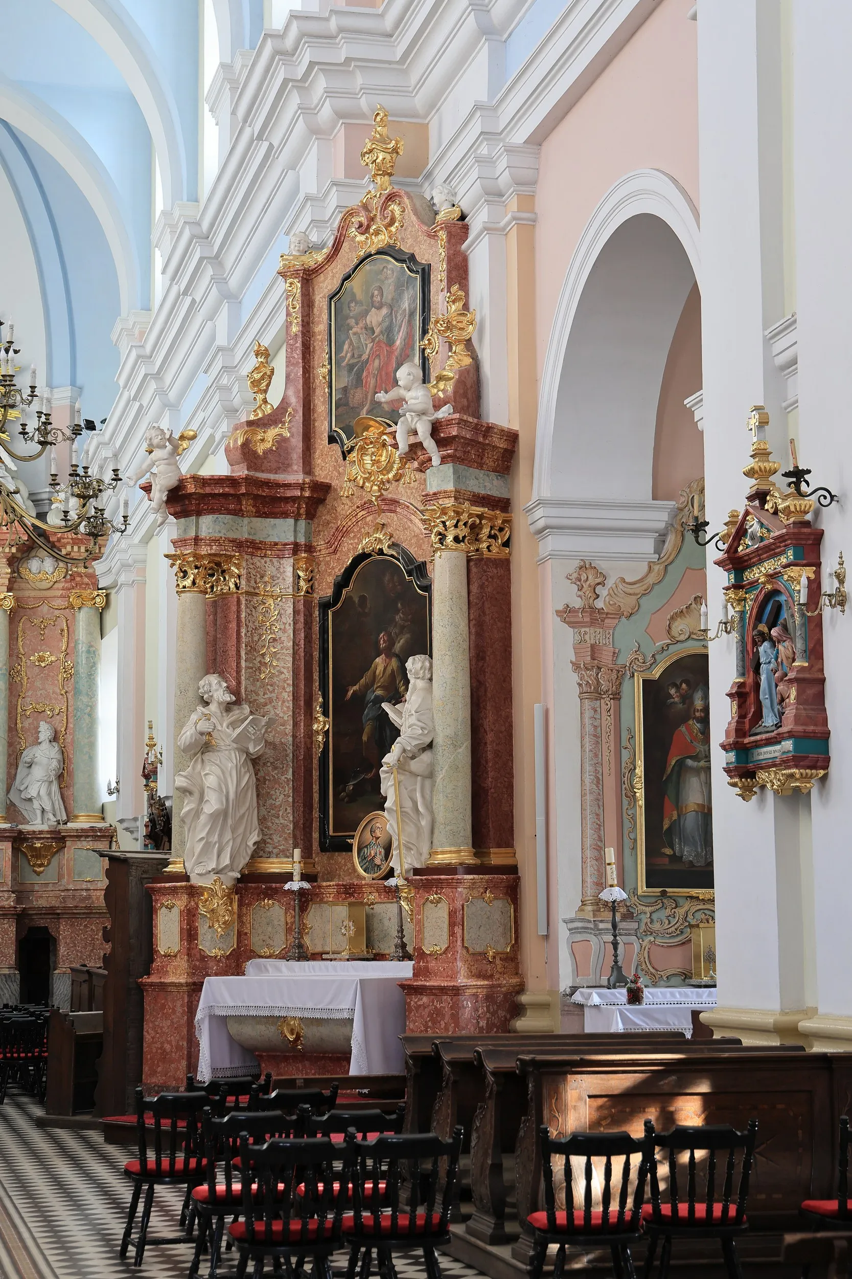 Barokowy boczny ołtarz z obrazami, rzeźbami i złoconymi zdobieniami. Przed ołtarzem ustawiono krzesła, a wnętrze rozświetla światło wpadające przez okna.