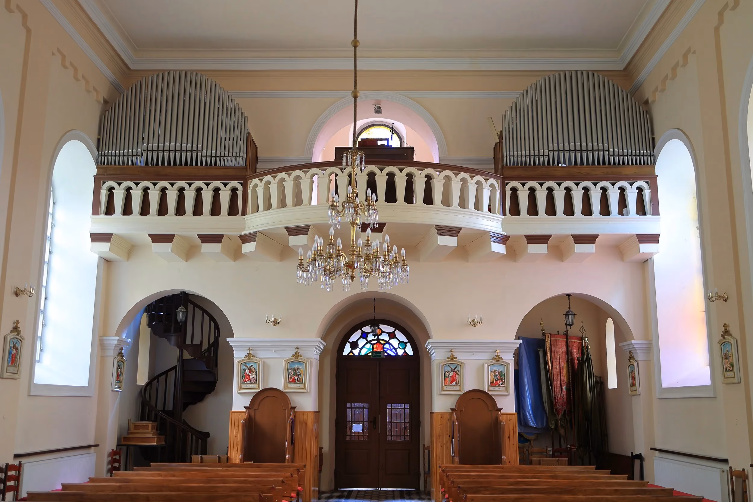 Widok na chór muzyczny z organami we wnętrzu kościoła. Pod balkonem znajdują się wejście główne, ławki i spiralne schody.