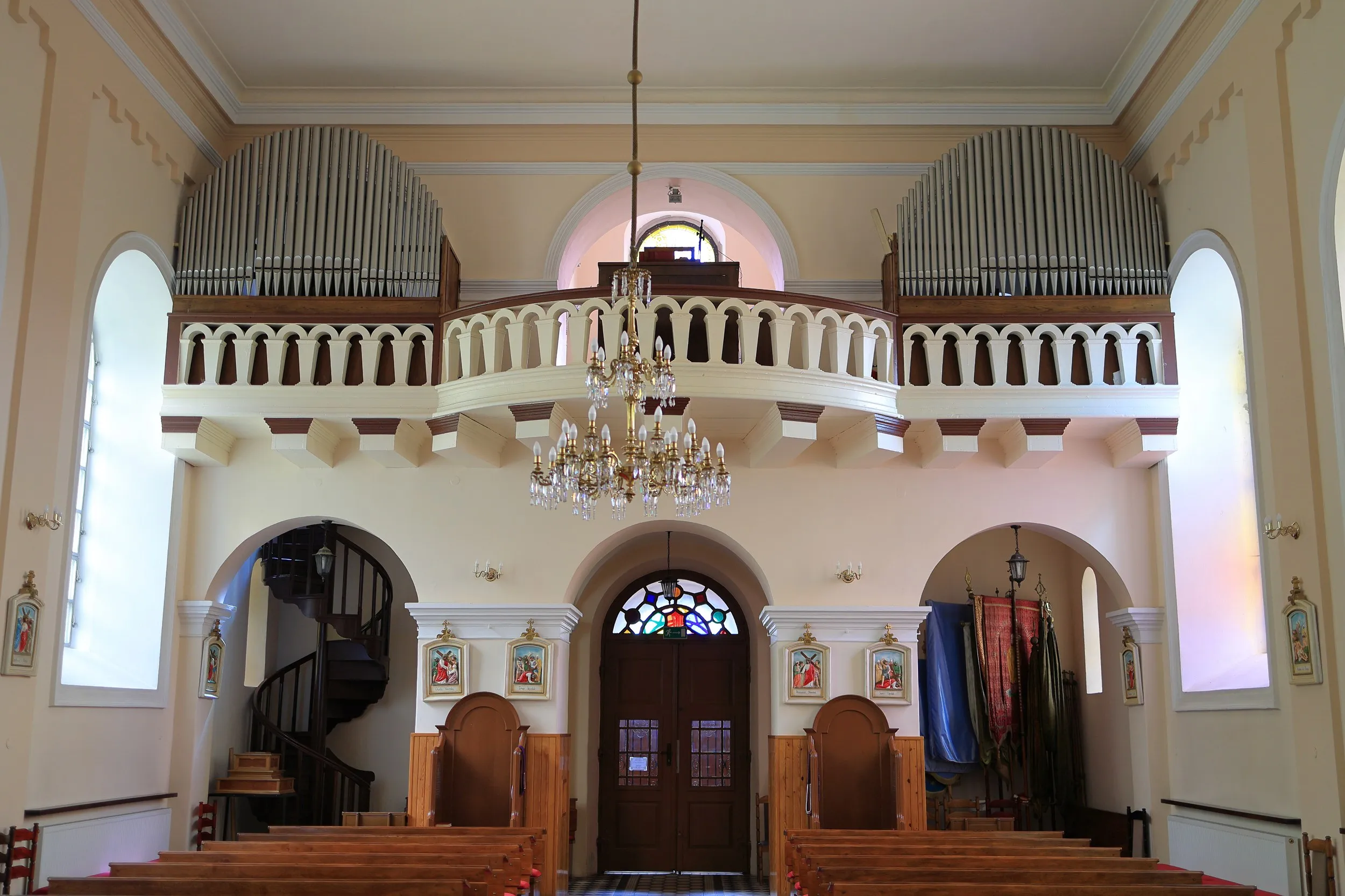Widok na chór muzyczny z organami we wnętrzu kościoła. Pod balkonem znajdują się wejście główne, ławki i spiralne schody.