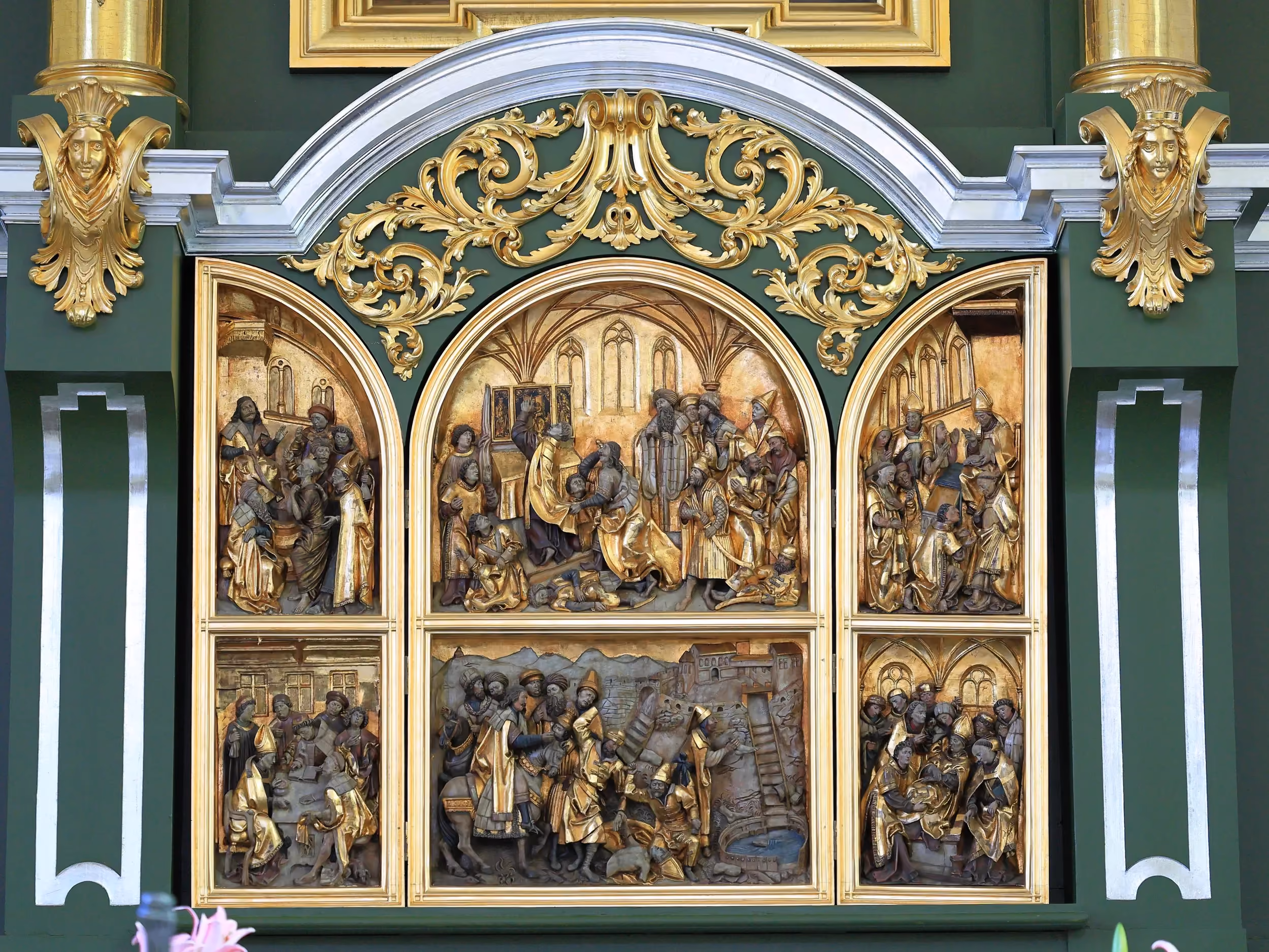 Gotycki ołtarz z sześcioma płaskorzeźbionymi scenami religijnymi. Całość otacza bogato zdobiona, zielono-złota oprawa.