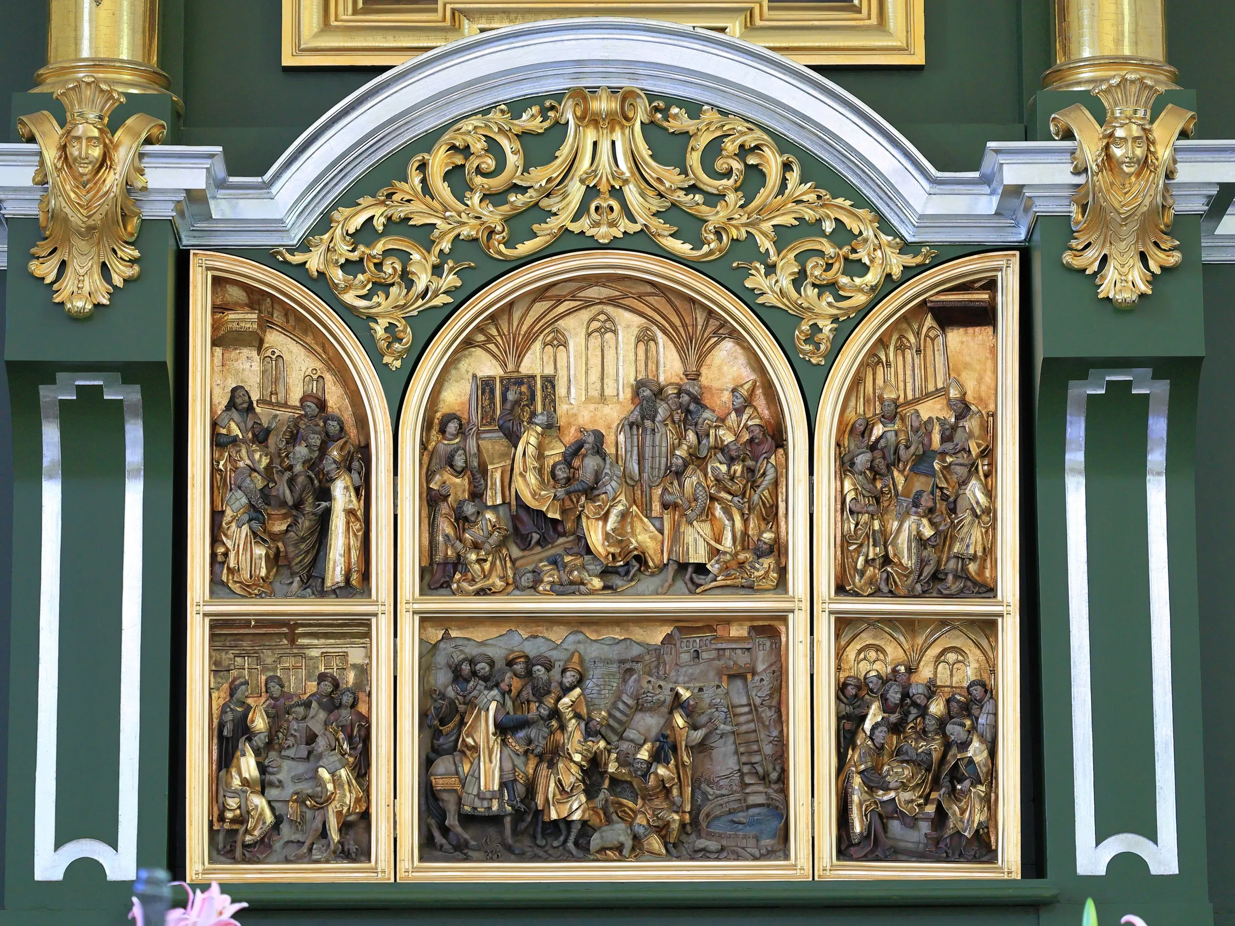 Gotycki ołtarz z sześcioma płaskorzeźbionymi scenami religijnymi. Całość otacza bogato zdobiona, zielono-złota oprawa.