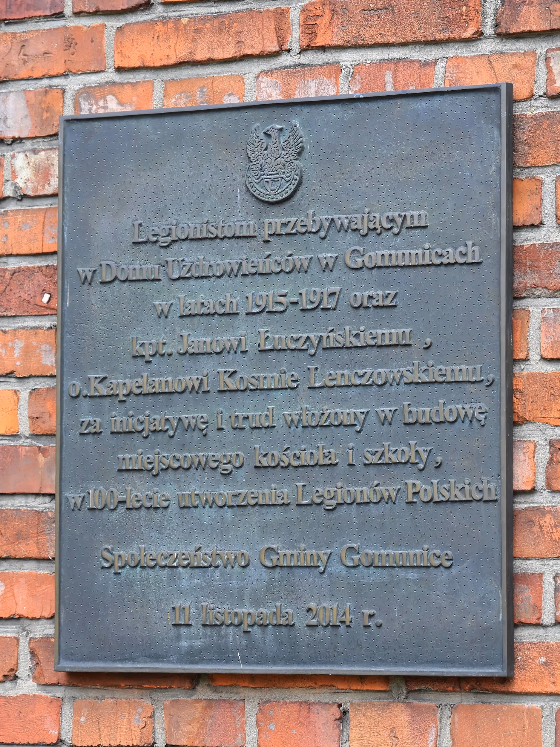Pamiątkowa tablica zamocowana na ceglanej ścianie kościoła. Upamiętnia legionistów przebywających w Gomunicach oraz osoby zasłużone dla budowy miejscowego kościoła i szkoły.