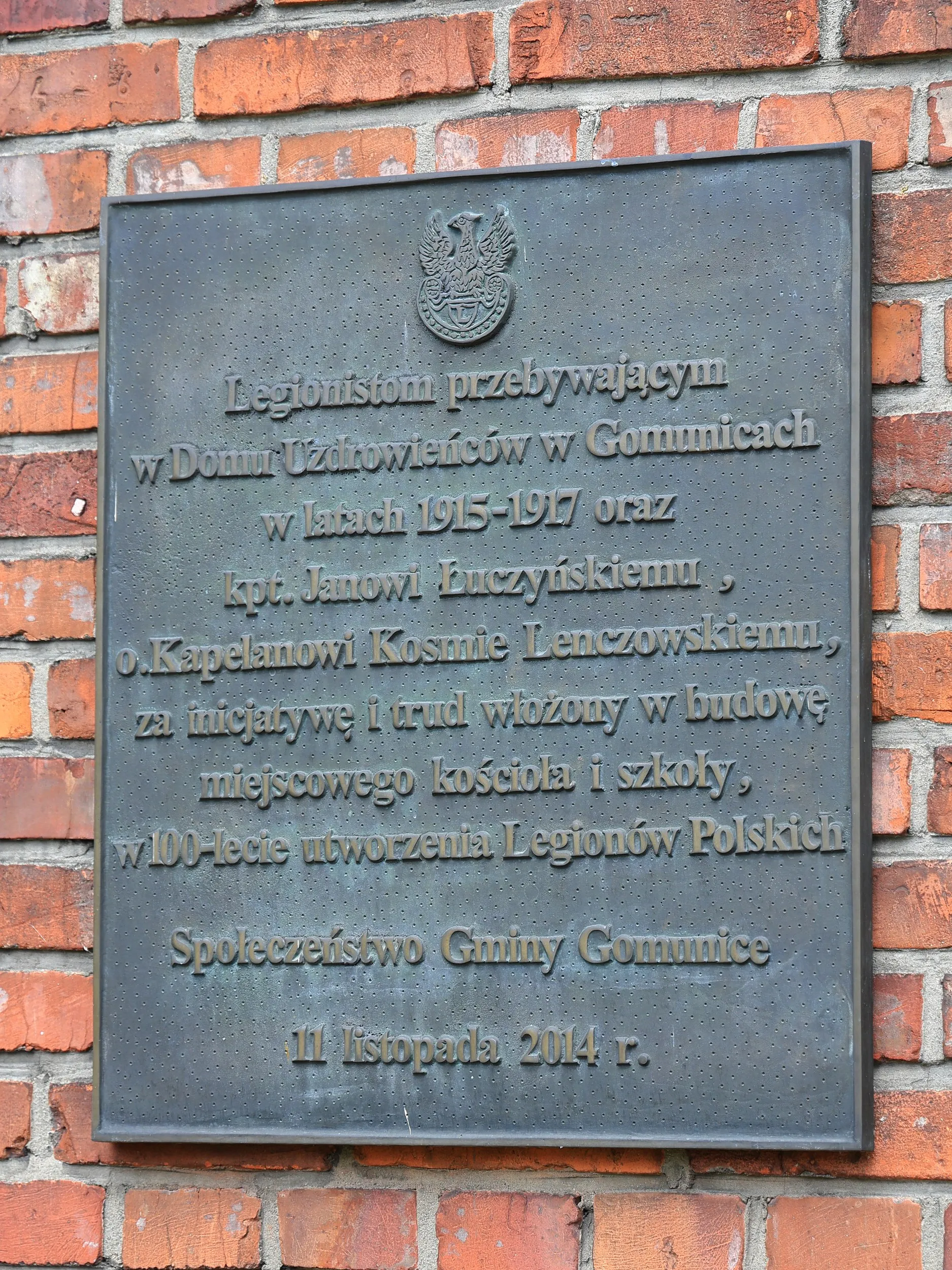 Pamiątkowa tablica zamocowana na ceglanej ścianie kościoła. Upamiętnia legionistów przebywających w Gomunicach oraz osoby zasłużone dla budowy miejscowego kościoła i szkoły.