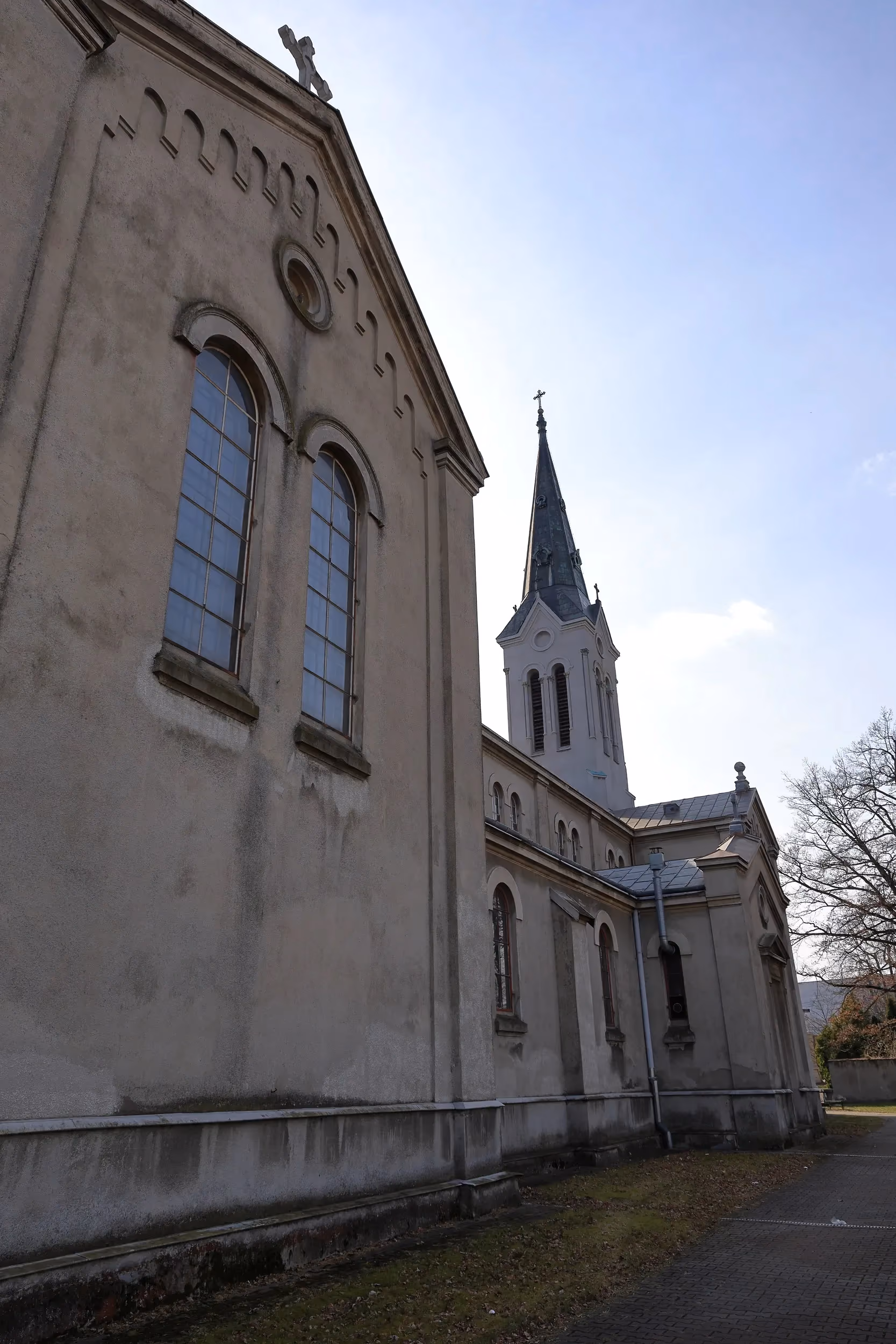 Fragment bocznej elewacji kościoła z wysokimi oknami i częścią wieży. Widoczne są detale architektoniczne oraz rynny.