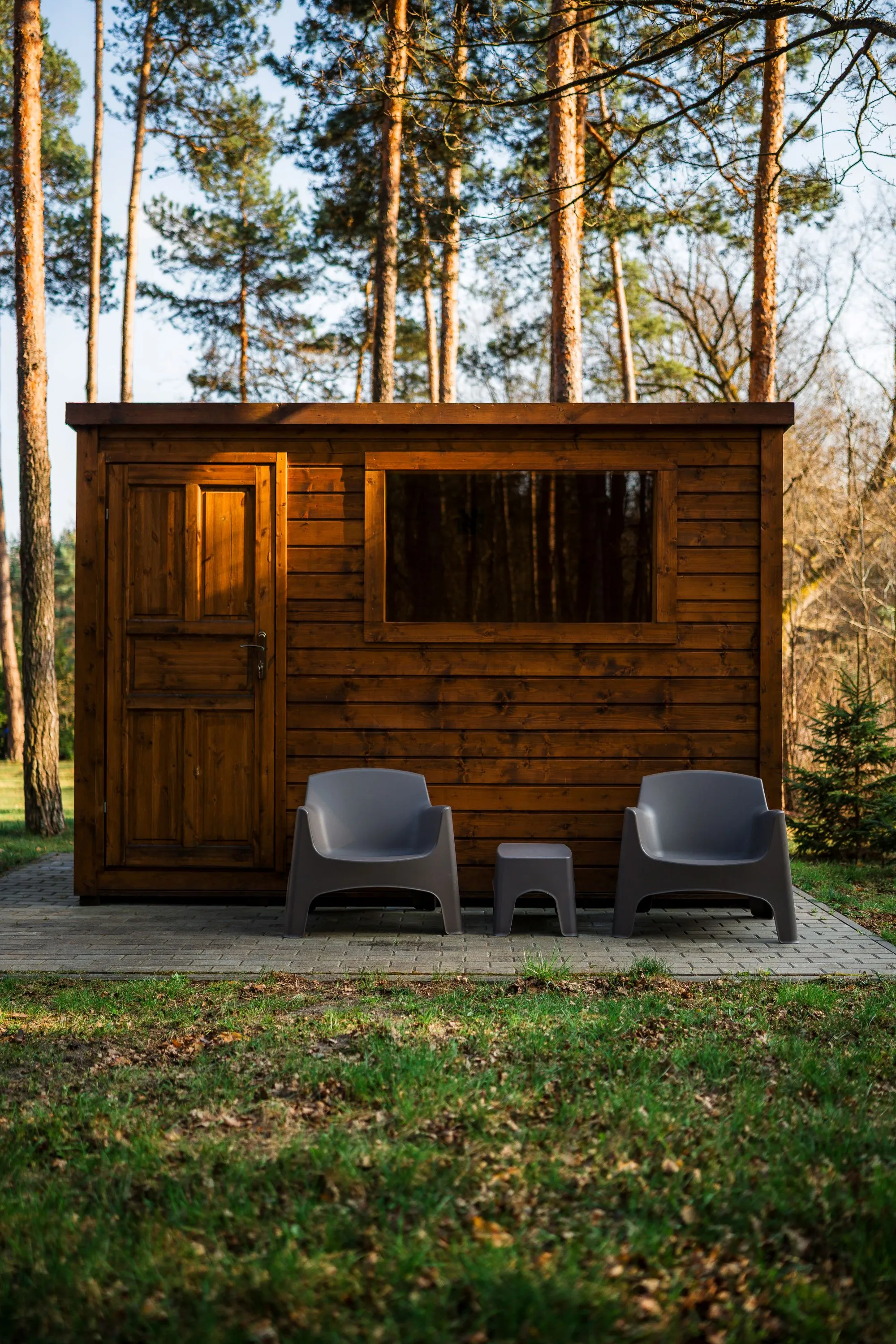 Drewniana sauna ogrodowa położona wśród sosen, zapewniająca prywatny wypoczynek blisko natury.