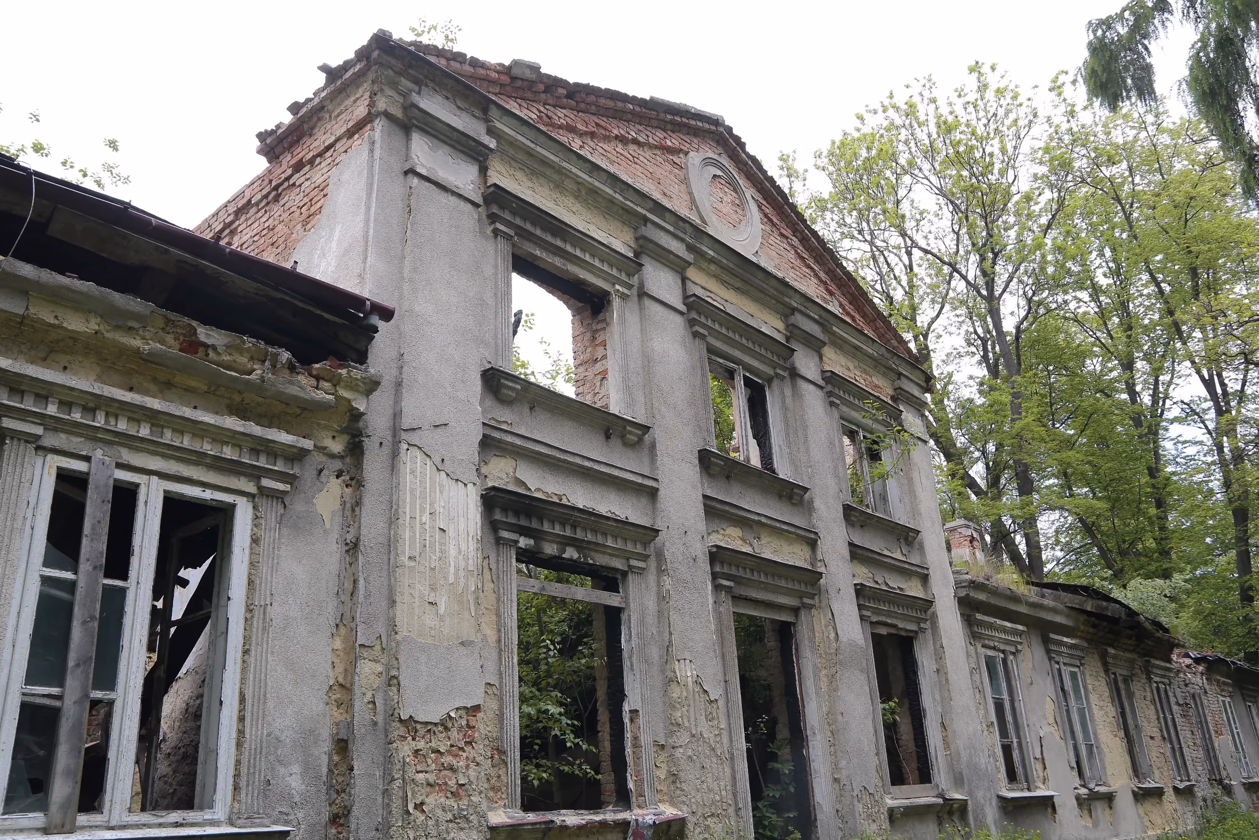 Zbliżenie na środkową część fasady dworu Tymowskich. Zachowane detale architektoniczne kontrastują z licznymi śladami zniszczeń.