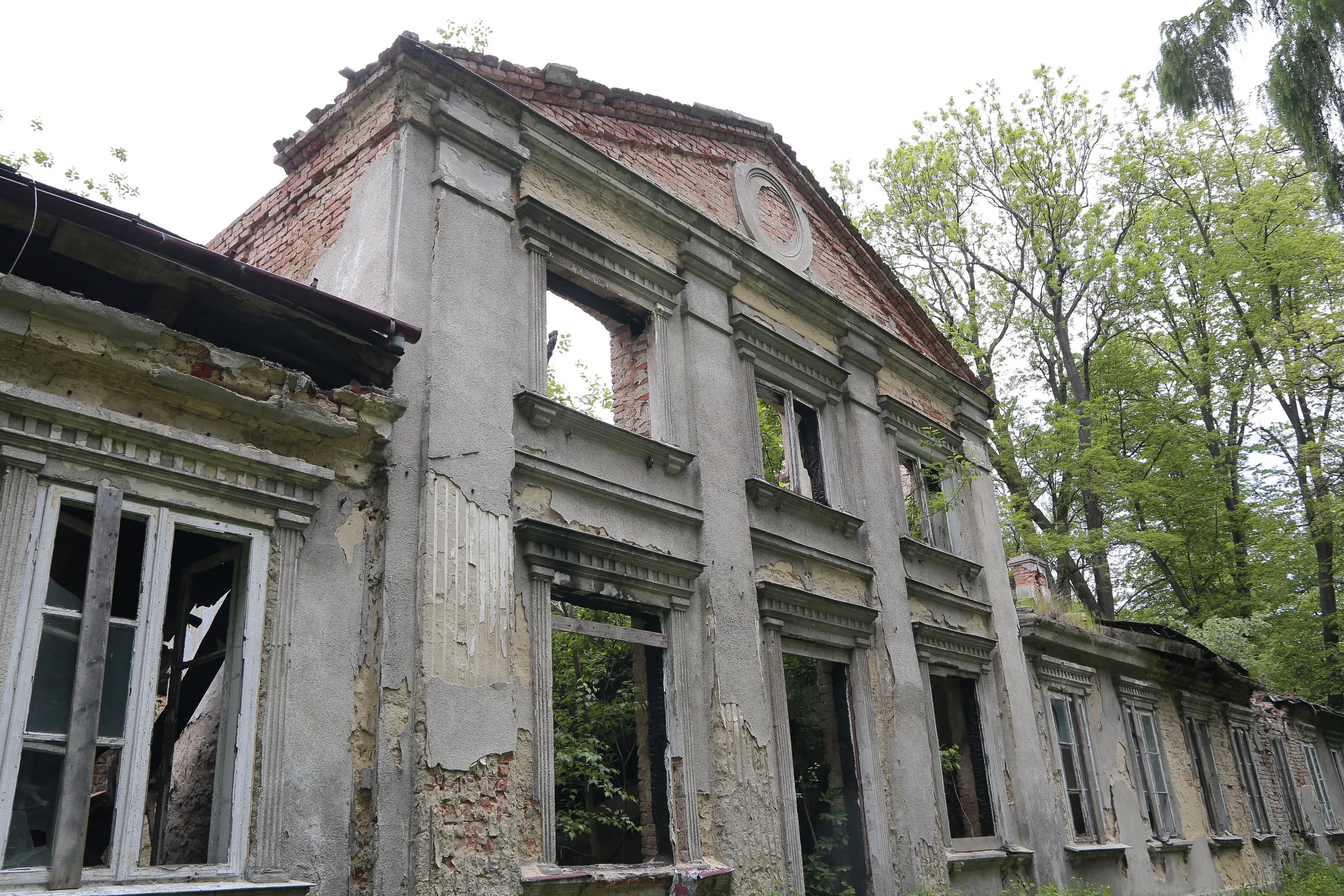 Zbliżenie na środkową część fasady dworu Tymowskich. Zachowane detale architektoniczne kontrastują z licznymi śladami zniszczeń.