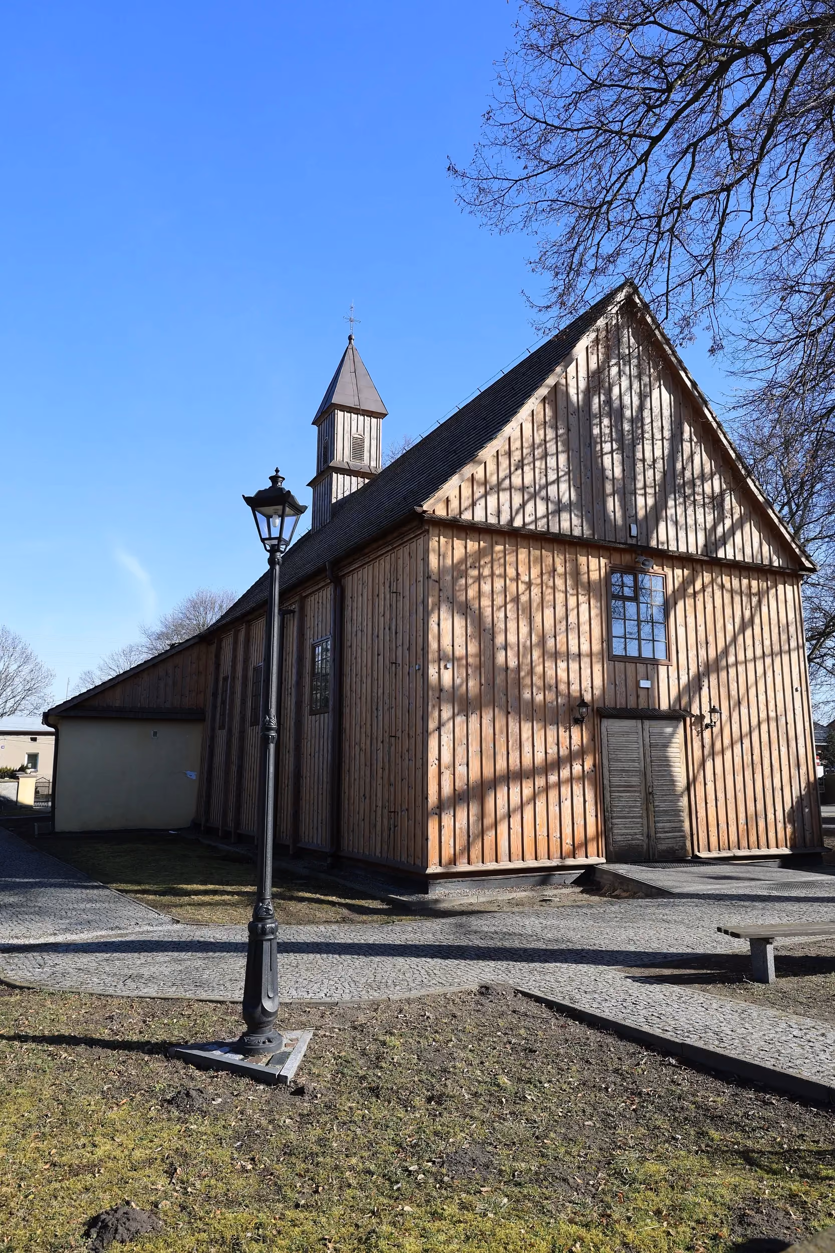 Widok kościoła w Rzejowicach od strony bocznej, drewniana bryła świątyni i wieżyczka na tle nieba.
