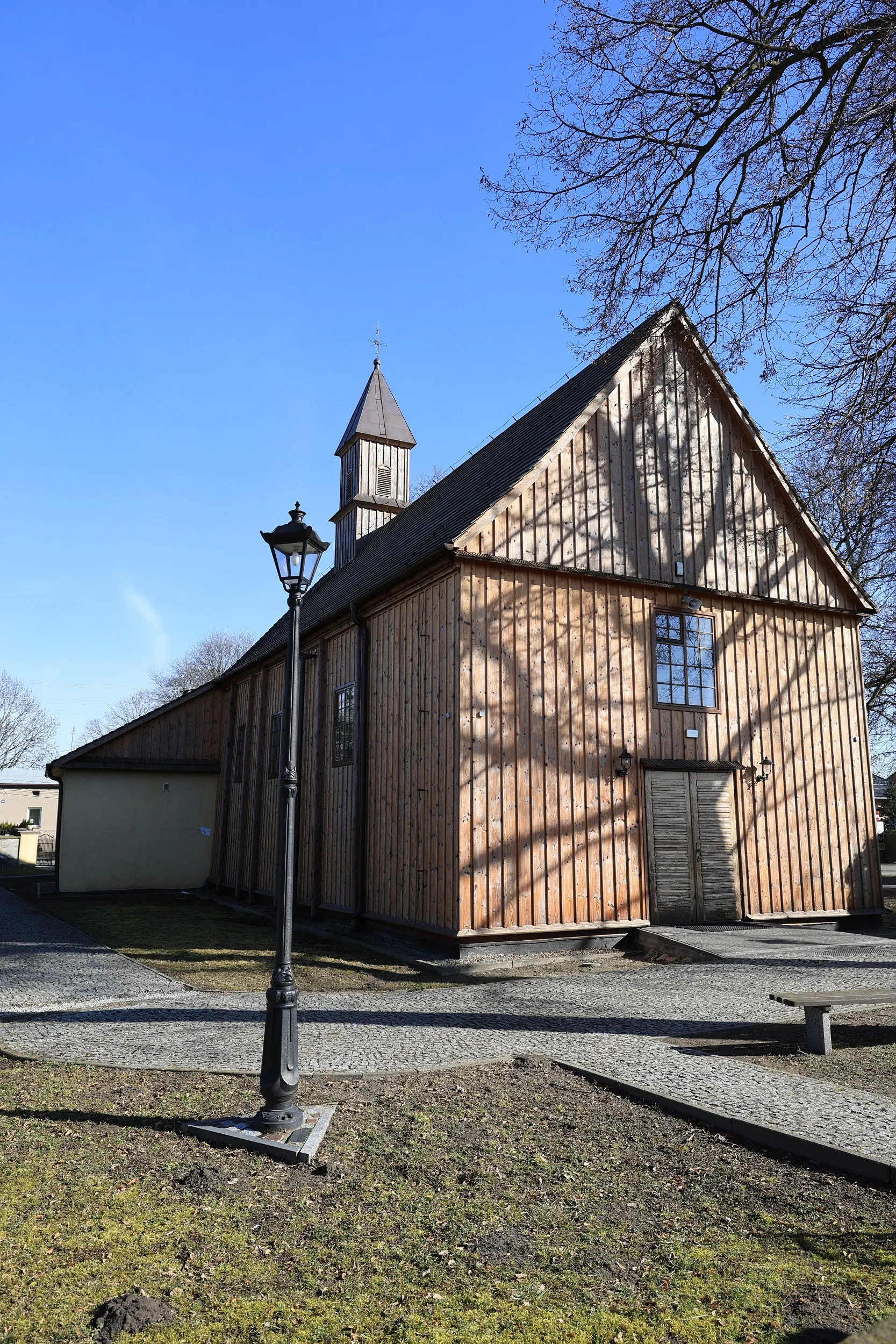 Widok kościoła w Rzejowicach od strony bocznej, drewniana bryła świątyni i wieżyczka na tle nieba.