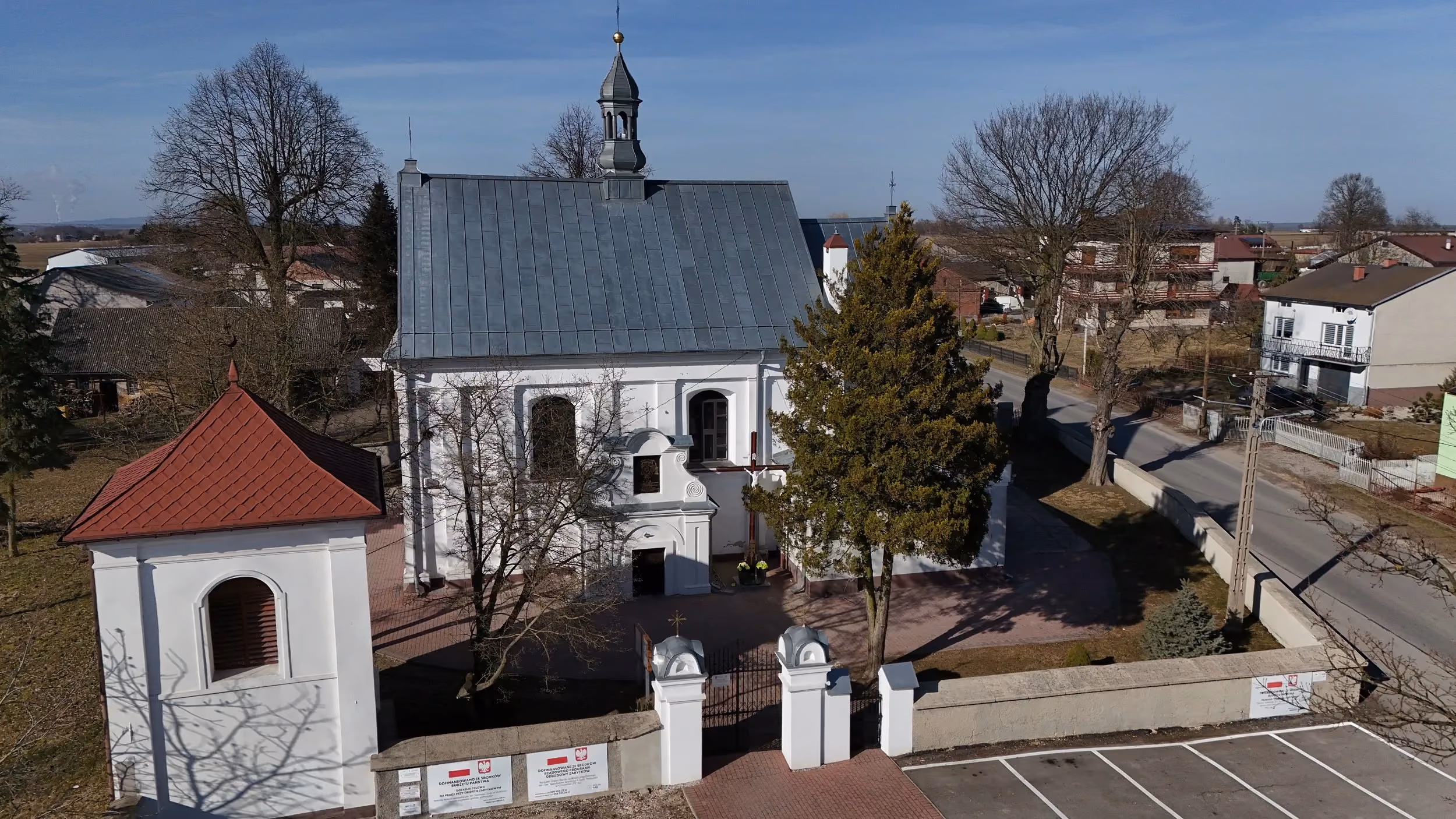 Widok z lotu ptaka na kościół w Dmeninie, dzwonnicę, ogrodzenie oraz najbliższe otoczenie świątyni.