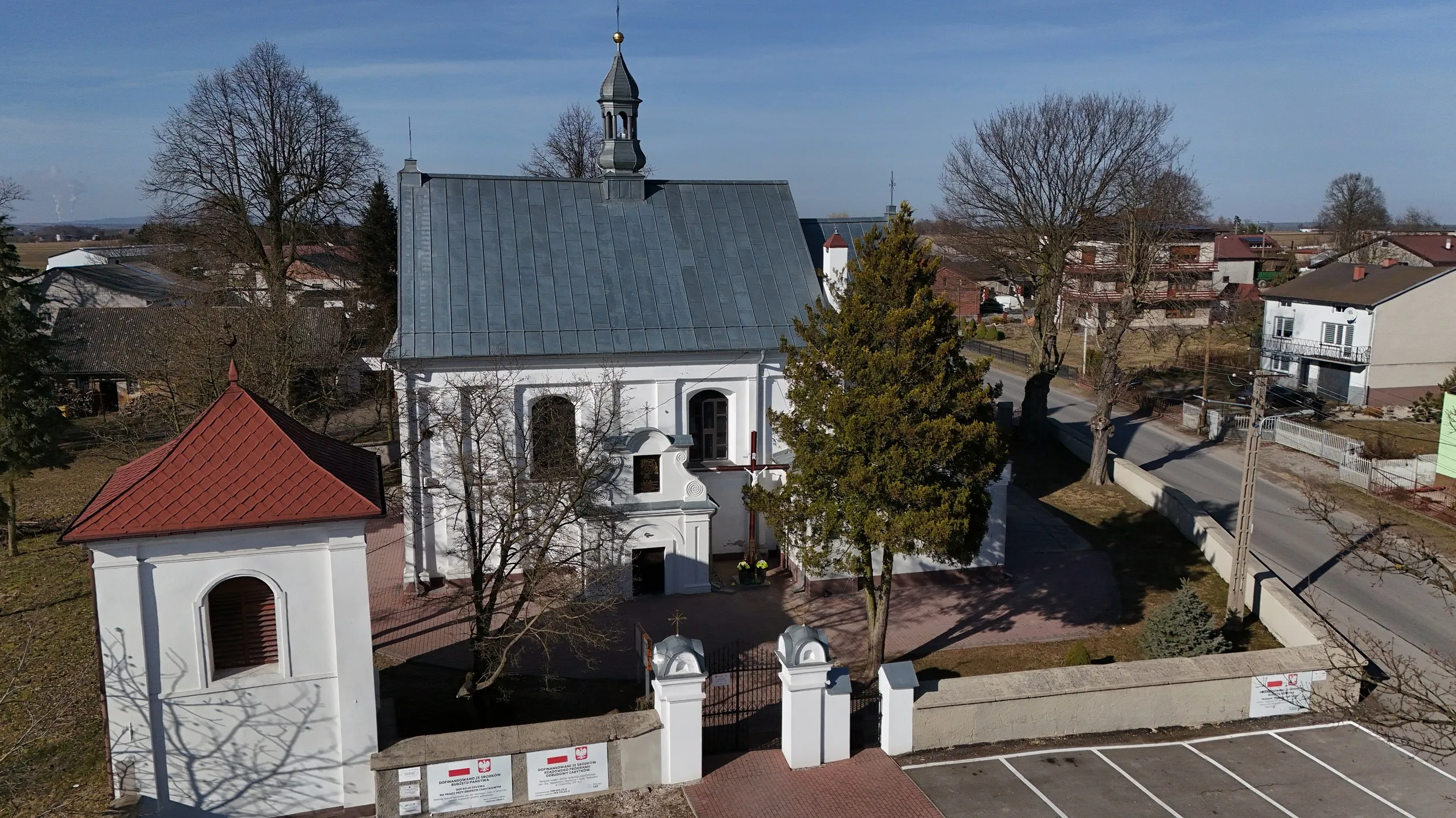 Widok z lotu ptaka na kościół w Dmeninie, dzwonnicę, ogrodzenie oraz najbliższe otoczenie świątyni.