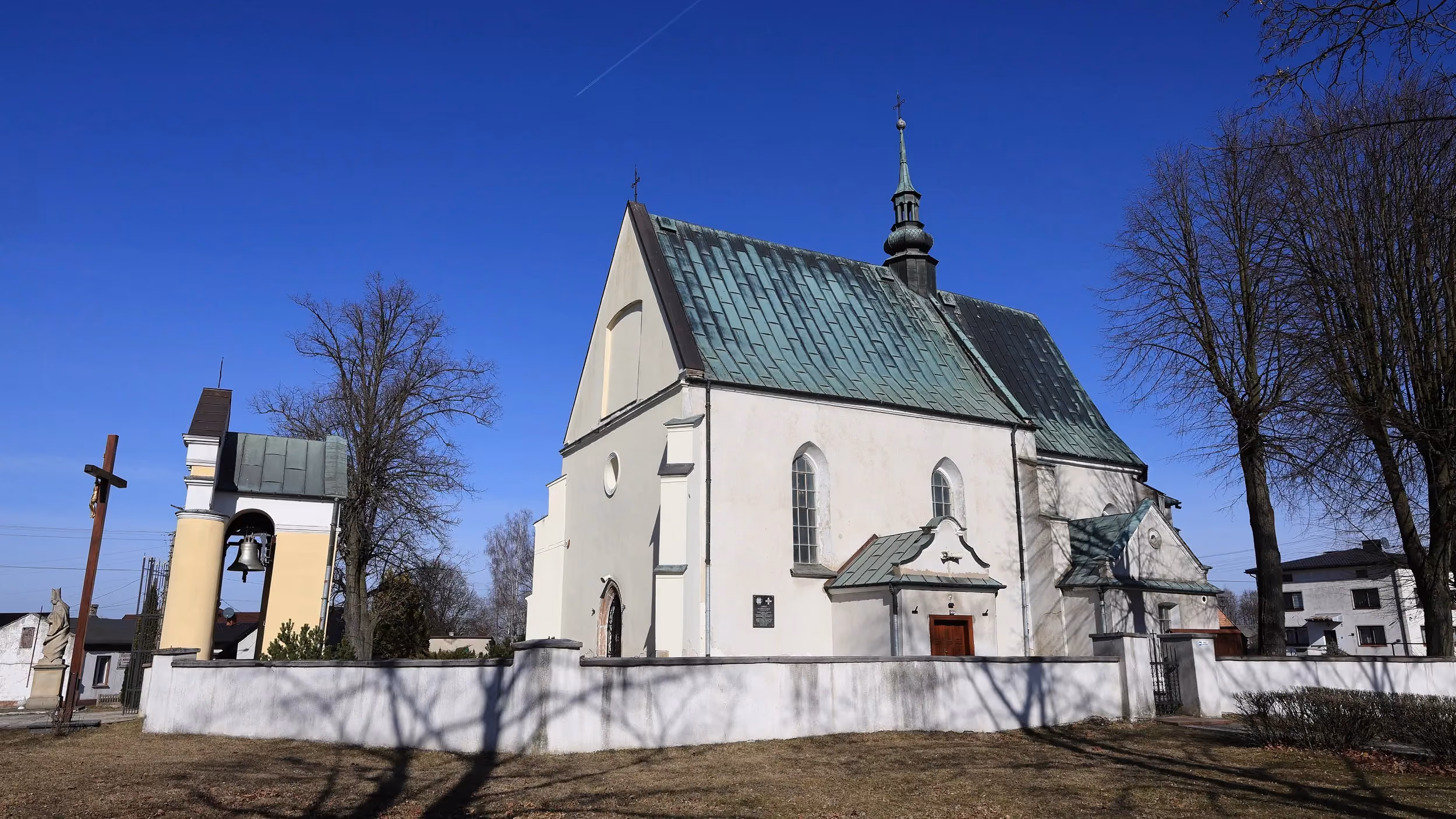 Kościół pw. św. Marcina w Kodrębie widziany z boku. Widoczna dzwonnica-brama, mur otaczający teren oraz dach pokryty blachą