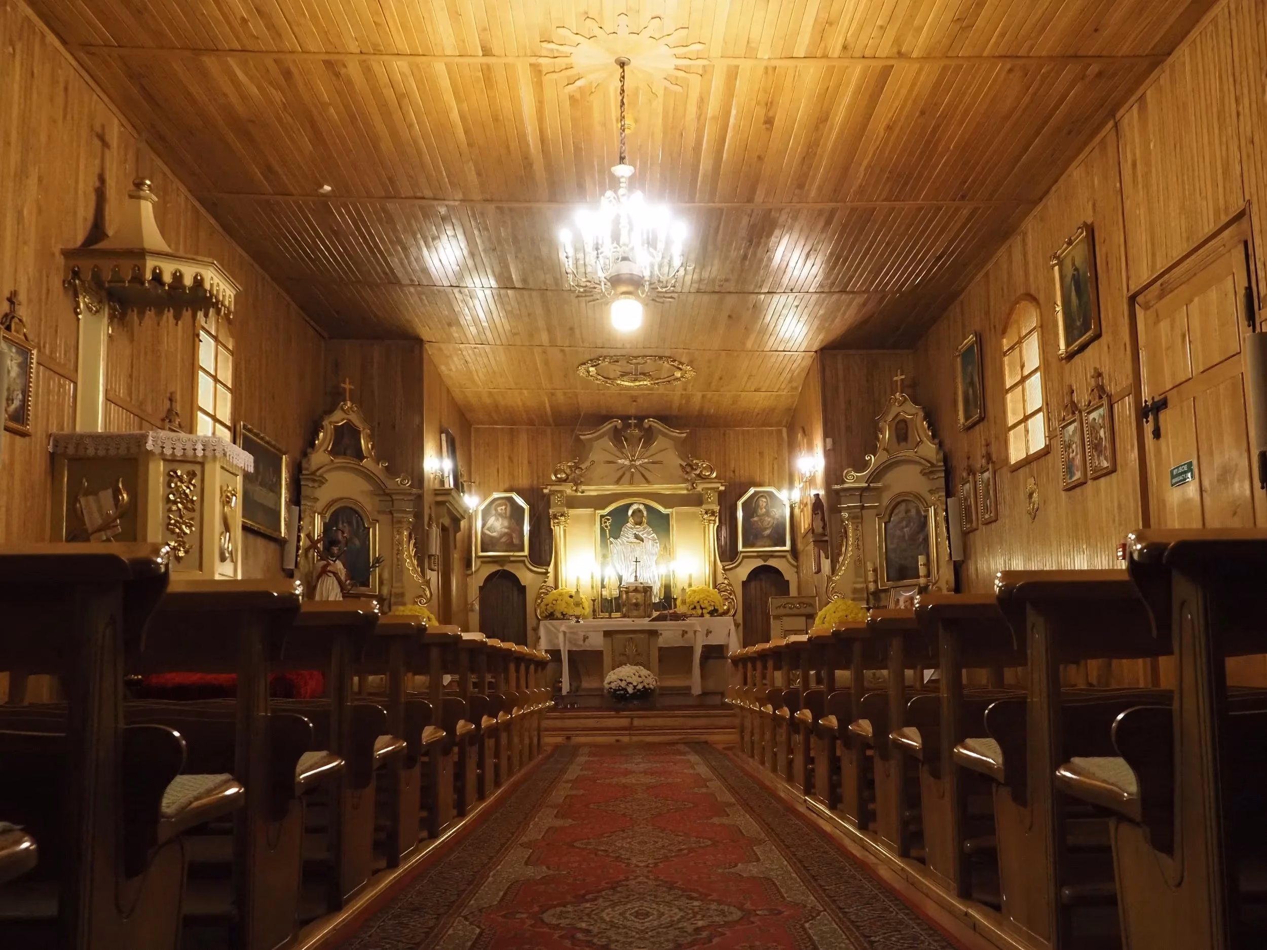 Wnętrze kościoła w Bugaju Zakrzewskim. Widok na nawę główną z drewnianymi ławkami i ołtarzem głównym.