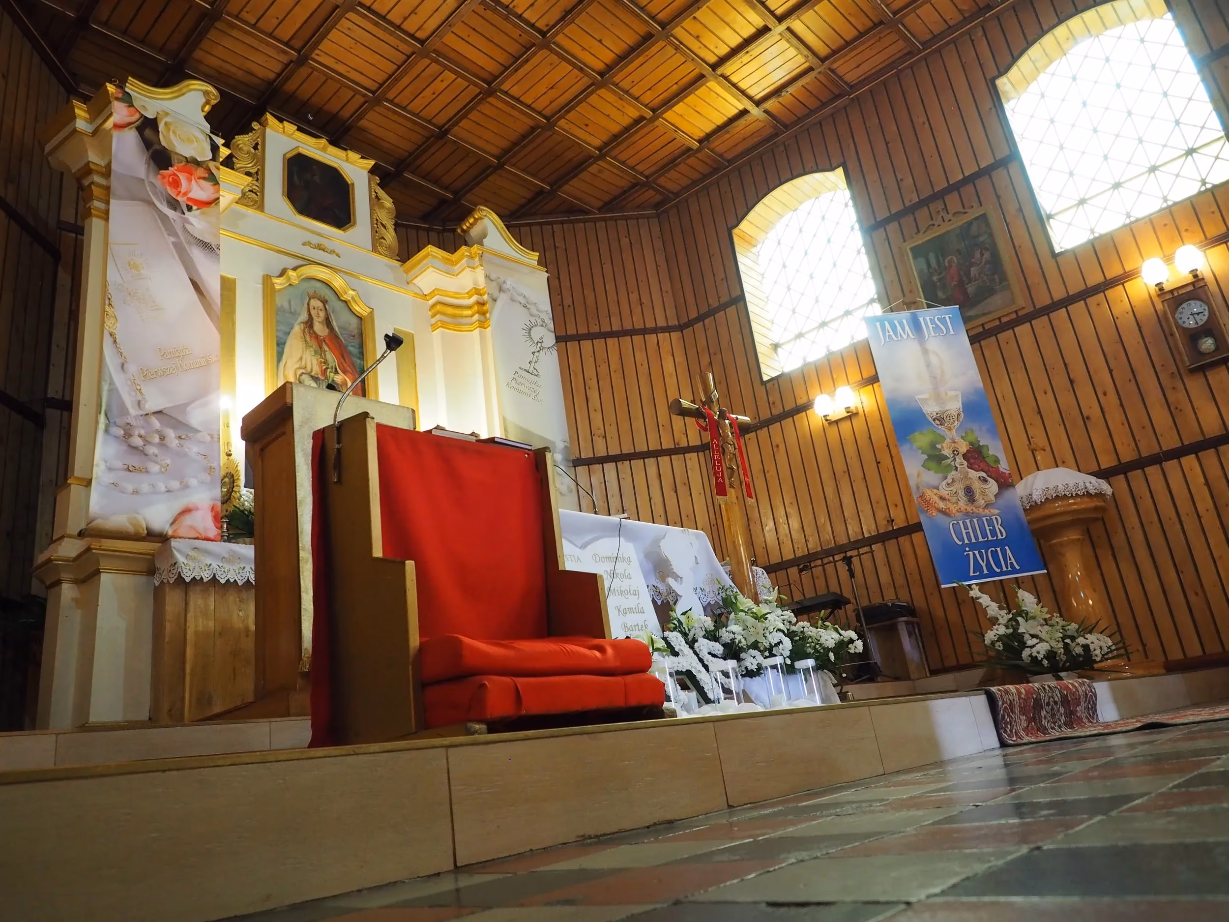Prezbiterium kościoła w Krępie z ołtarzem, amboną i dekoracjami liturgicznymi. Wysokie okna doświetlają drewniane wnętrze świątyni.