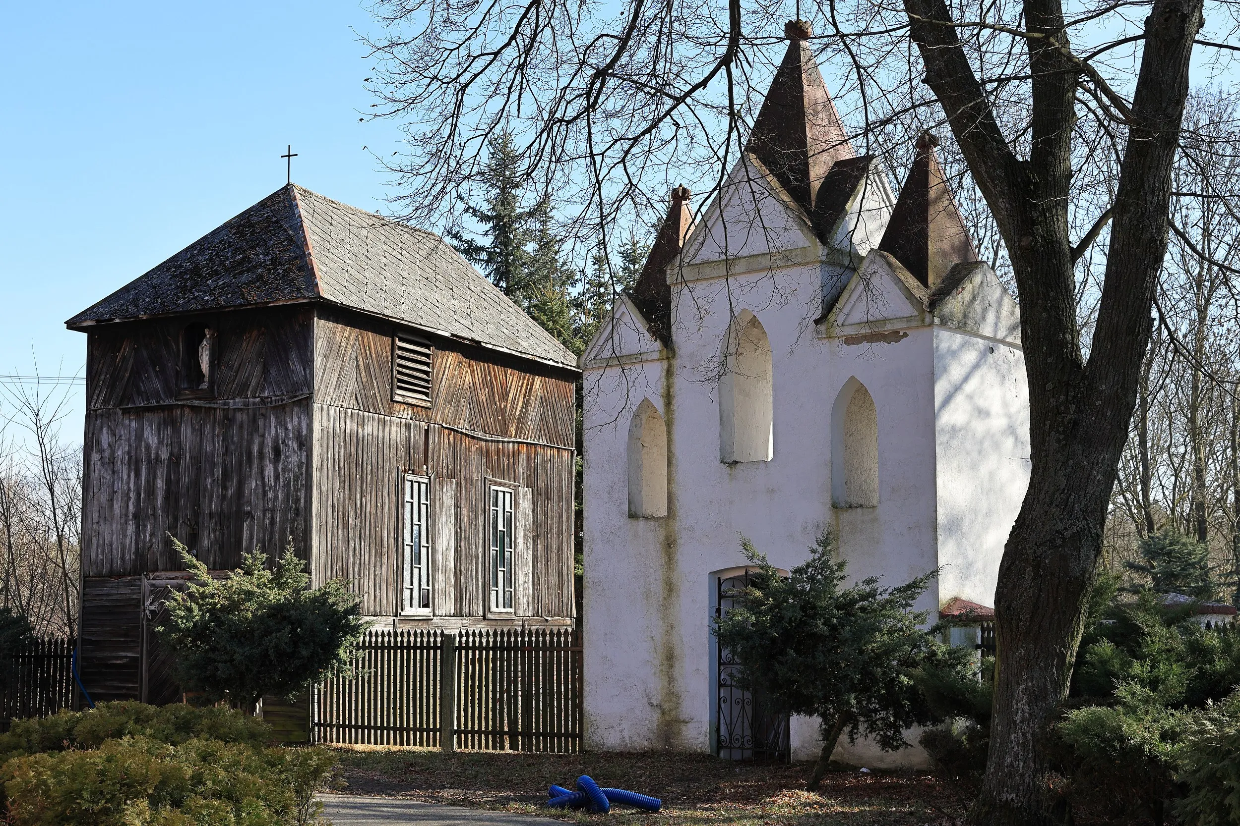 Drewniana dzwonnica i zabytkowa murowana dzwonnica przy kościele w Krępie. Obiekty otoczone są drzewami i ogrodzeniem na terenie przykościelnym.