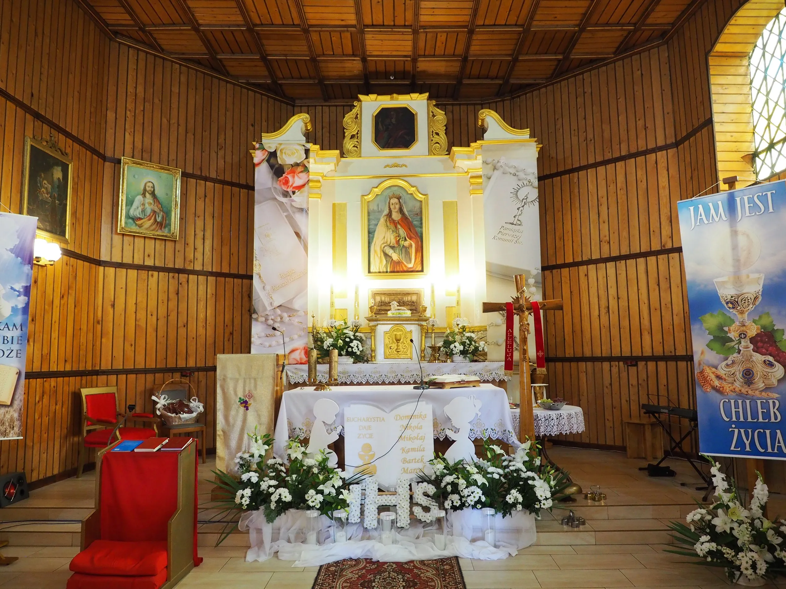 Wnętrze kościoła w Krępie z głównym ołtarzem. Widoczne dekoracje liturgiczne, kwiaty oraz obrazy religijne na drewnianych ścianach.