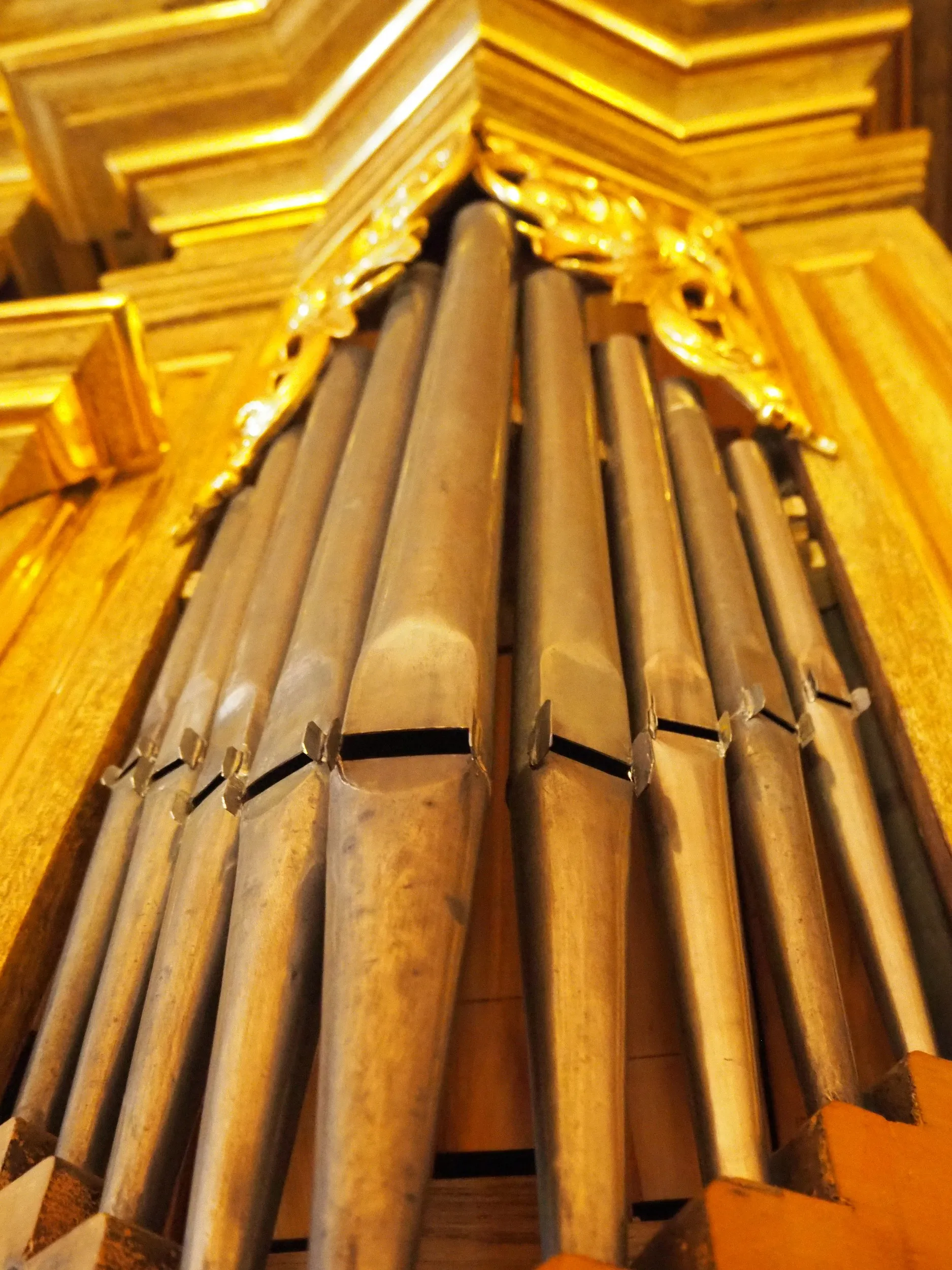 Zbliżenie na piszczałki organowe we wnętrzu kościoła w Lgocie Wielkiej. Metalowe elementy otoczone są złoconymi zdobieniami.