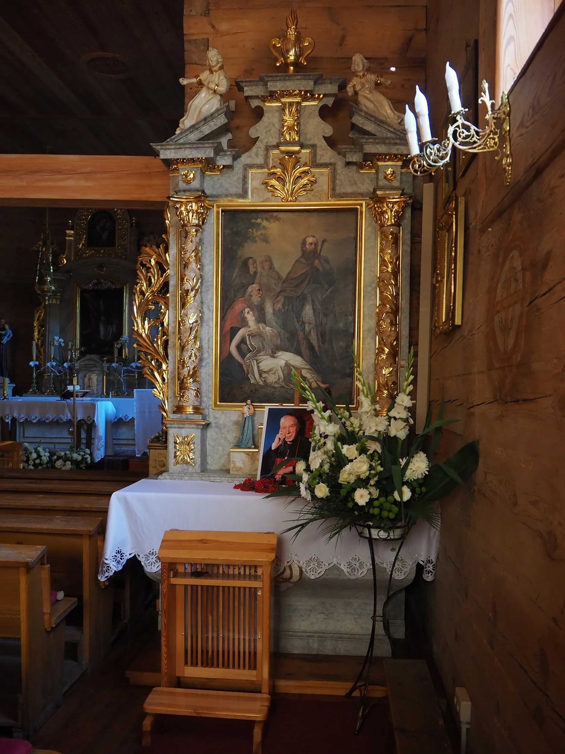 Boczny ołtarz w kościele w Lgocie Wielkiej. Zdobiona nastawa ołtarzowa z obrazem religijnym i kompozycją kwiatową.