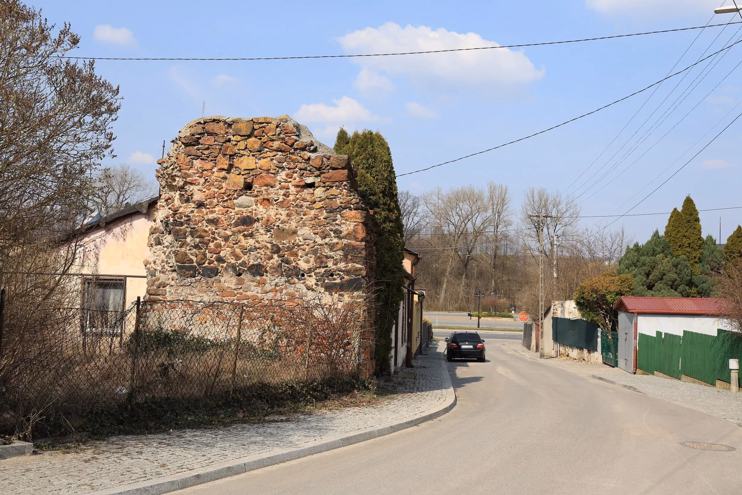 Relikt zamku w Przedborzu – zachowany fragment kamiennego muru obronnego przy ulicy. Widoczne nieregularne kamienie spojone zaprawą oraz zabudowa miejska w tle.