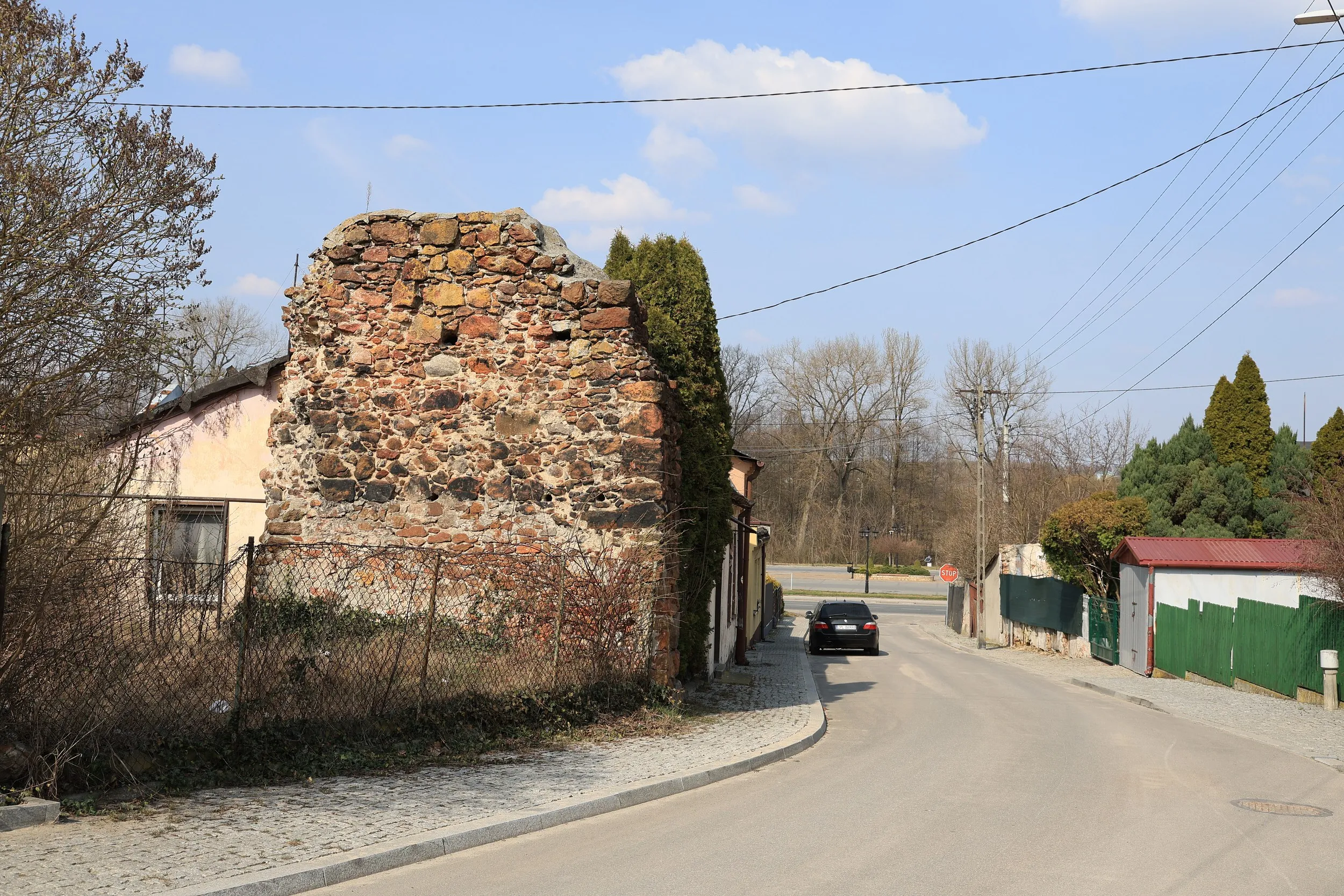 Relikt zamku w Przedborzu – zachowany fragment kamiennego muru obronnego przy ulicy. Widoczne nieregularne kamienie spojone zaprawą oraz zabudowa miejska w tle.