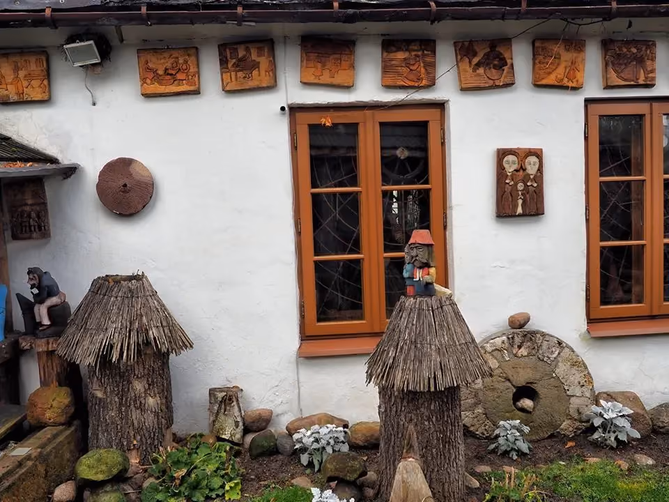 Fragment elewacji Muzeum Ludowego Ziemi Przedborskiej. Widoczne drewniane dekoracje, eksponaty etnograficzne oraz elementy dawnego wyposażenia gospodarczego.