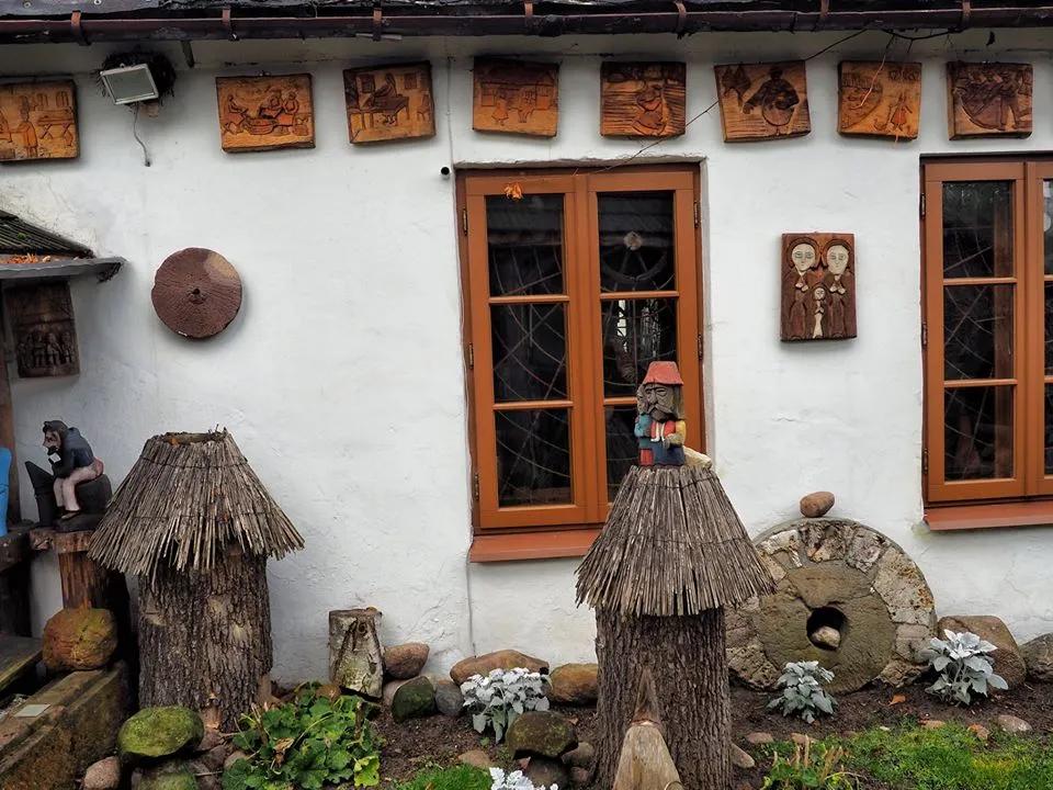 Fragment elewacji Muzeum Ludowego Ziemi Przedborskiej. Widoczne drewniane dekoracje, eksponaty etnograficzne oraz elementy dawnego wyposażenia gospodarczego.