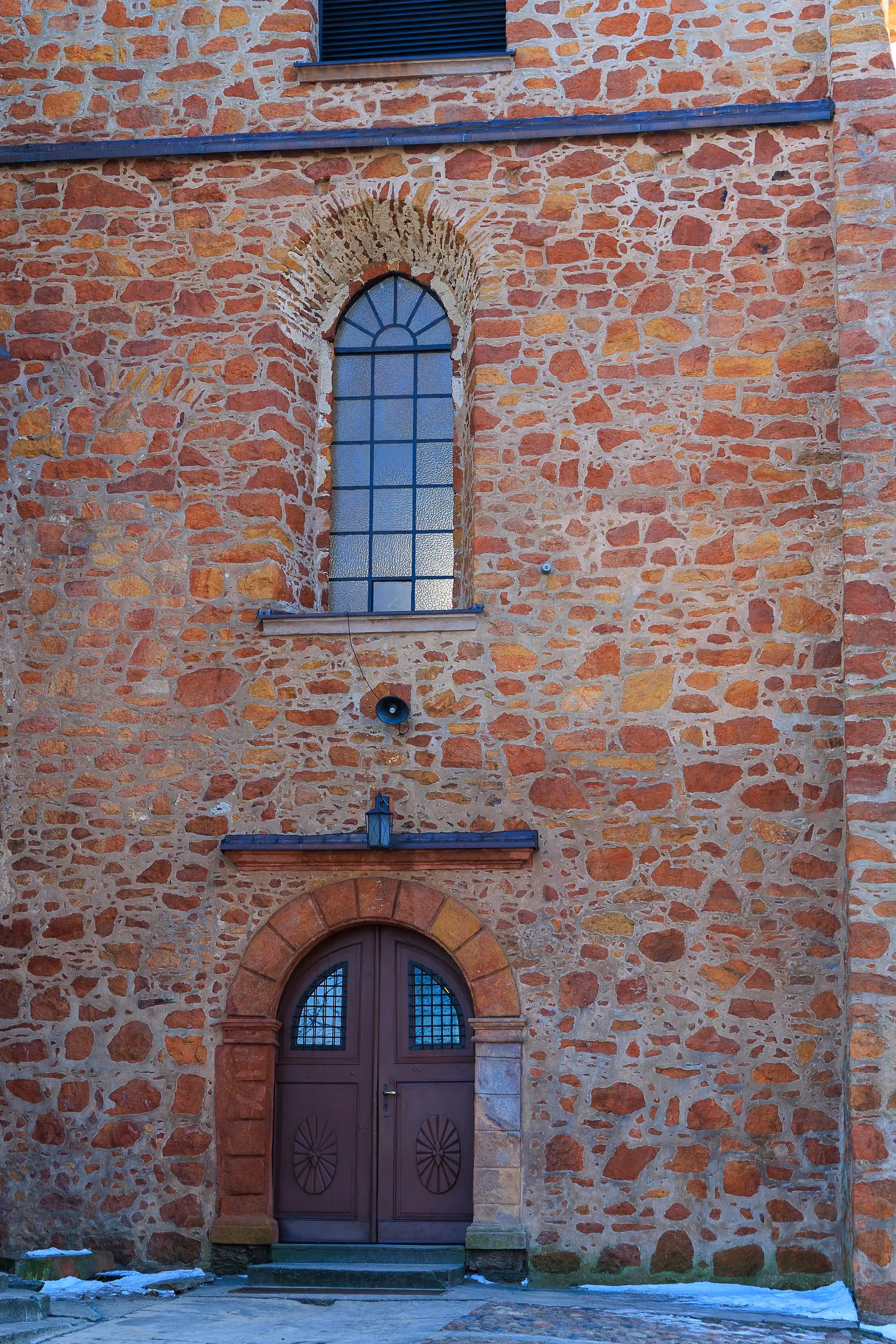 Wejście do ceglanej wieży kościoła św. Aleksego. Widoczne drewniane drzwi oraz wysokie okno z półkolistym zwieńczeniem.