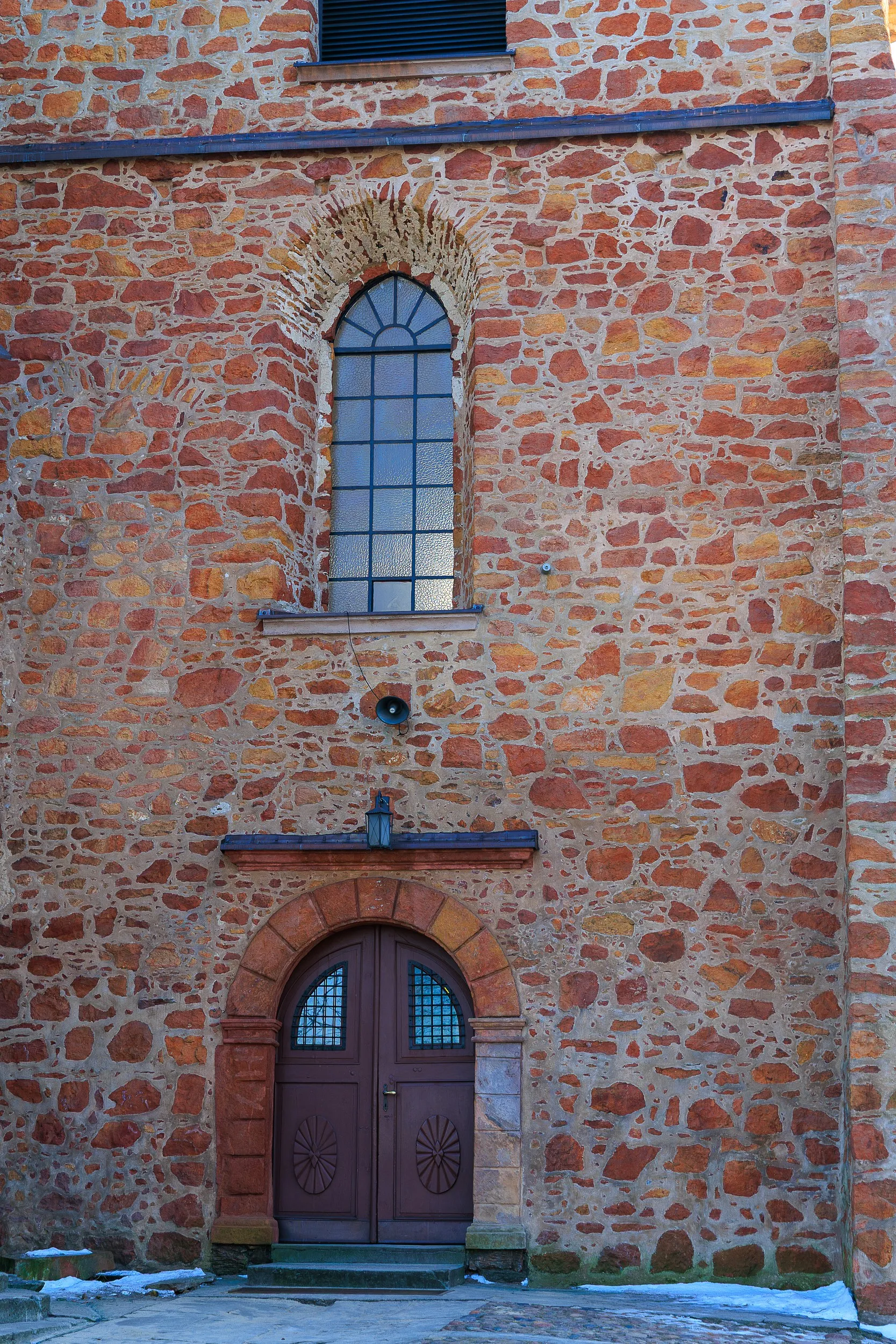 Wejście do ceglanej wieży kościoła św. Aleksego. Widoczne drewniane drzwi oraz wysokie okno z półkolistym zwieńczeniem.