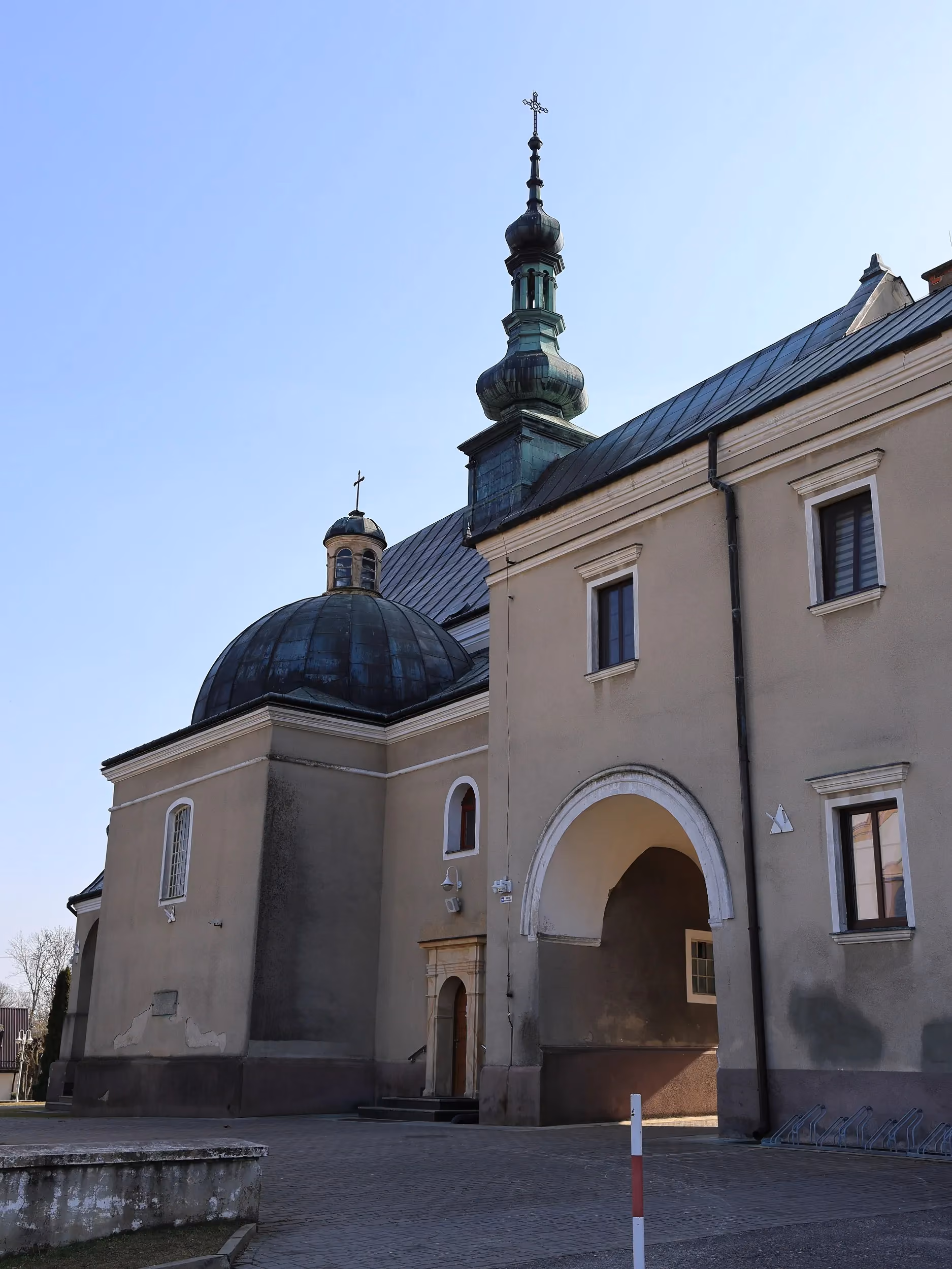Boczna elewacja kościoła w Wielgomłynach z kopułą i wieżą. Widoczne są arkadowe przejście oraz fragment dziedzińca.