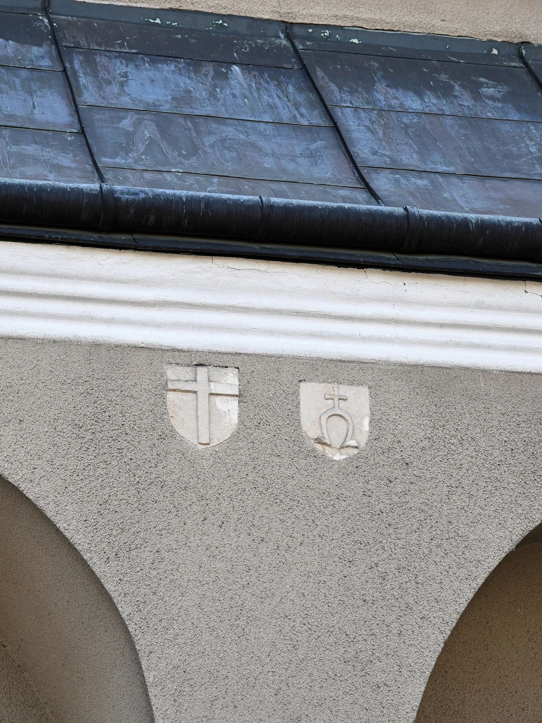 Detale architektoniczne kościoła w Wielgomłynach. Na ścianie widoczne są dwa kamienne herby umieszczone pod okapem dachu.