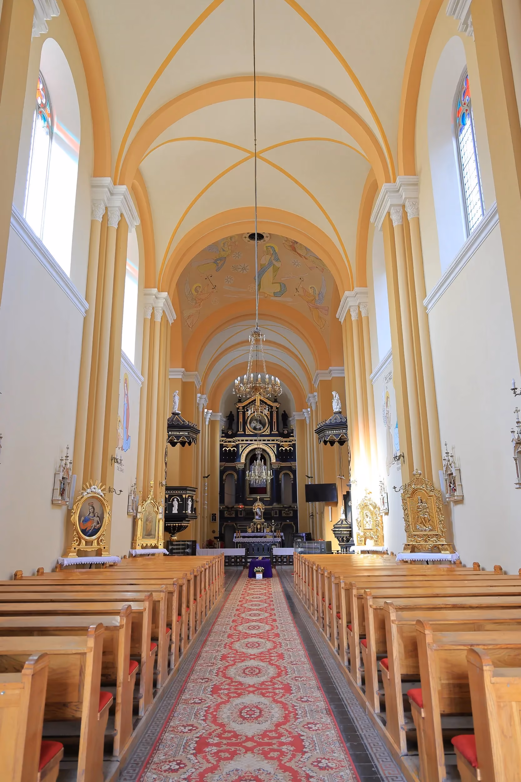 Wnętrze kościoła w Żytnie. Widok głównej nawy z drewnianymi ławkami, sklepieniem i ołtarzem w głębi świątyni.
