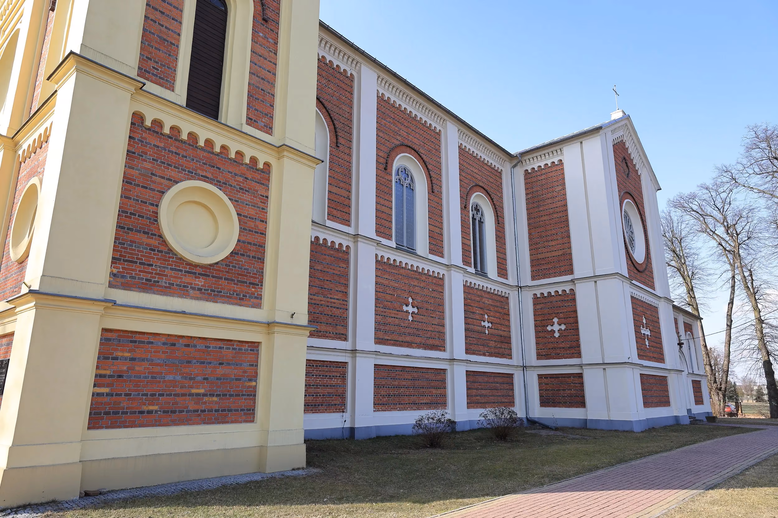 Boczna elewacja kościoła w Żytnie. Ceglano-tynkowana ściana z wysokimi oknami i ścieżką prowadzącą wzdłuż budynku.