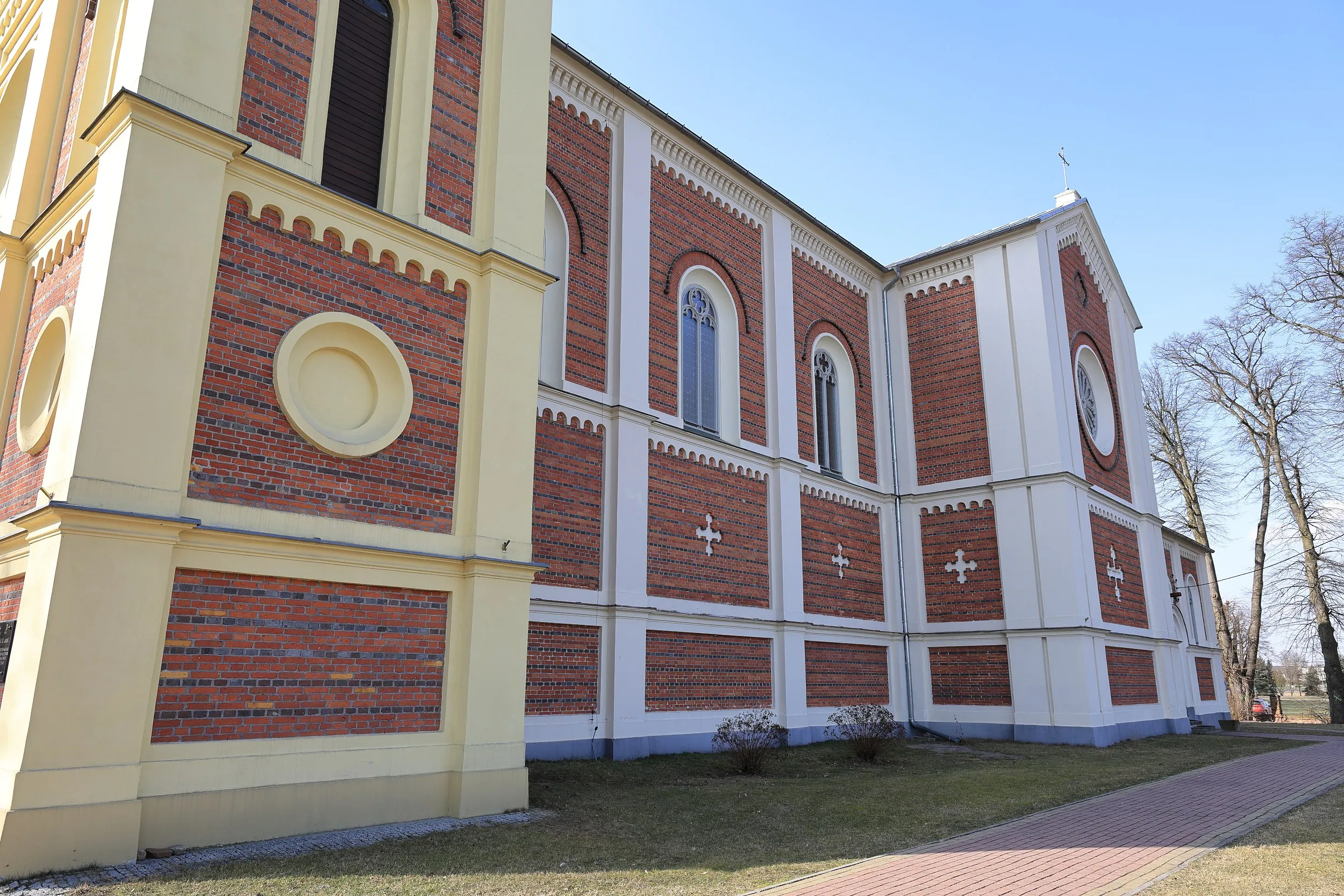 Boczna elewacja kościoła w Żytnie. Ceglano-tynkowana ściana z wysokimi oknami i ścieżką prowadzącą wzdłuż budynku.