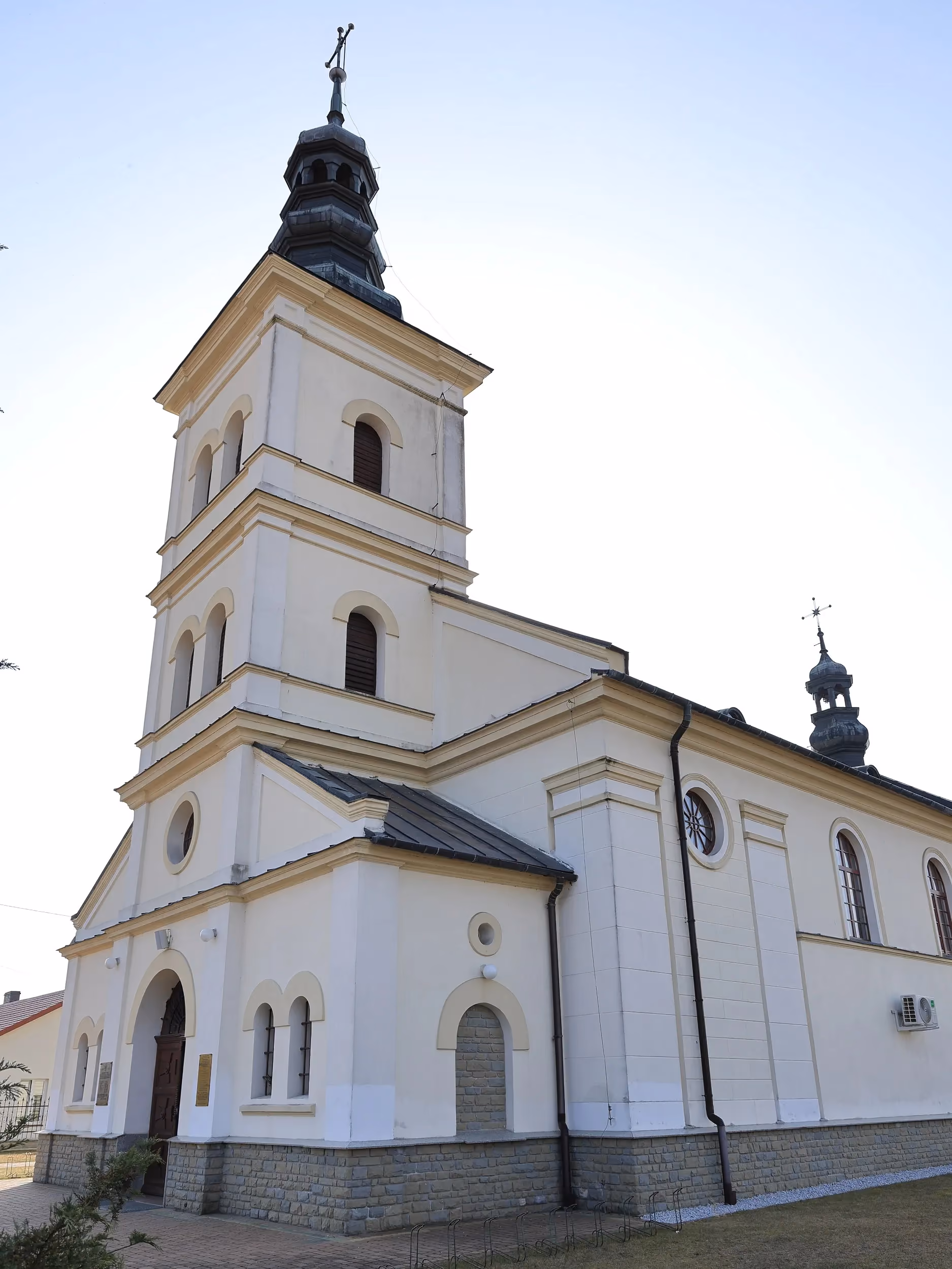 Widok kościoła w Borzykowej od strony bocznej. Jasna elewacja świątyni z wieżą, oknami i głównym wejściem.